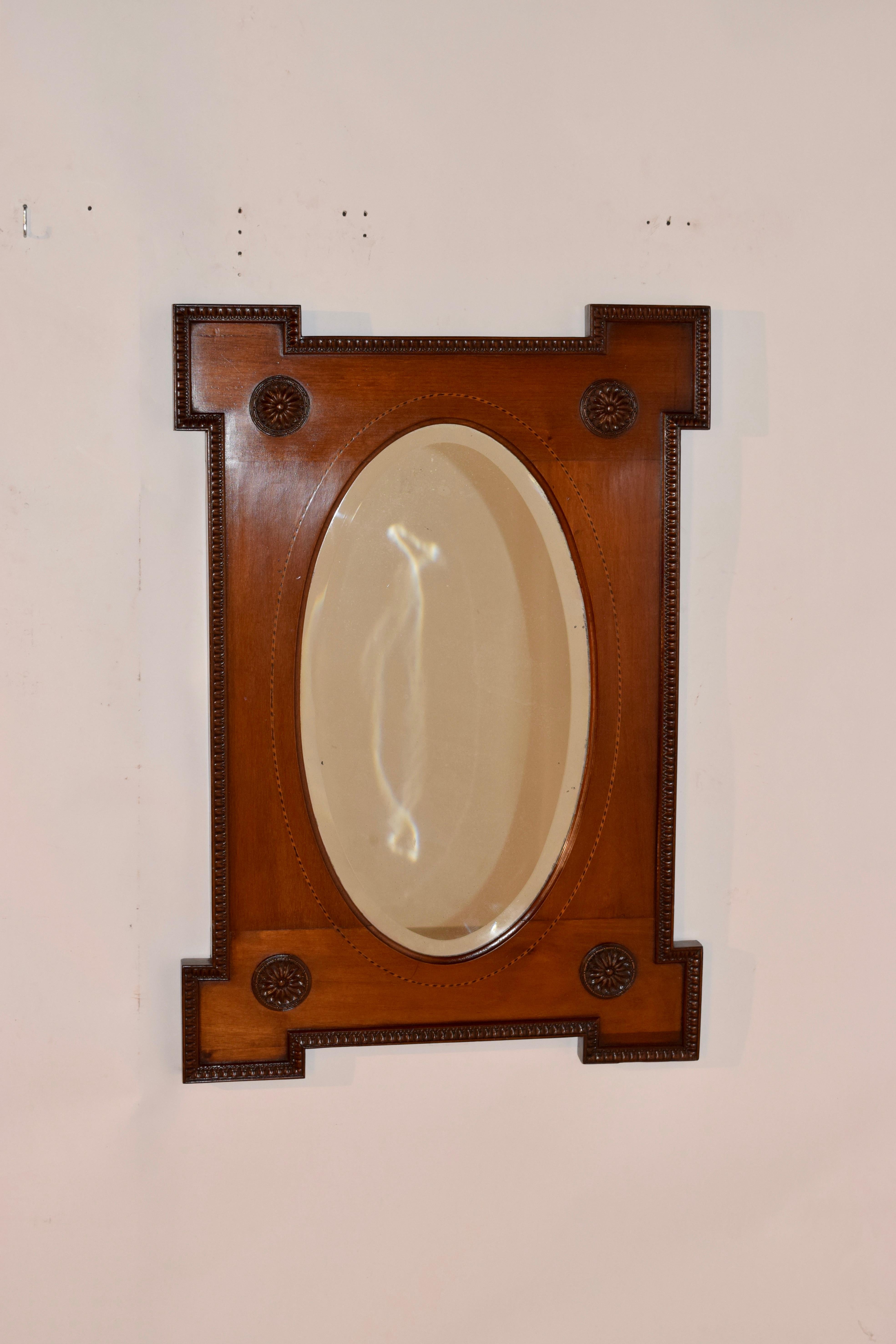 19th century English mirror made from mahogany. The mirror frame has a wonderfully hand carved molded edge, surrounding the oval beveled mirror, which has a banding of satinwood and ebony barber pole inlay. There are hand carved rosettes adorning