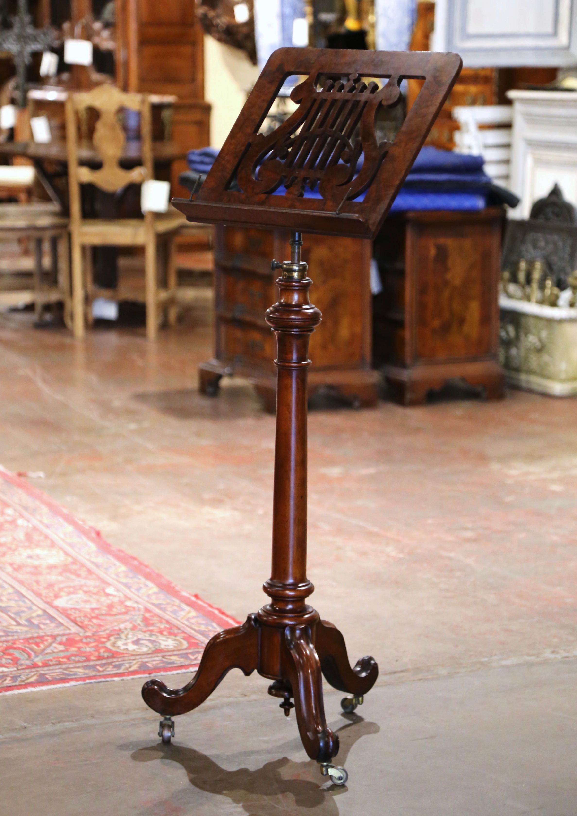 This elegant, antique lectern was crafted in England, circa 1870. The hand-carved music sheet holder stands on a three-leg wheeled pedestal base over a circular tapered stem; it is dressed with a swivel single side book stand decorated with a