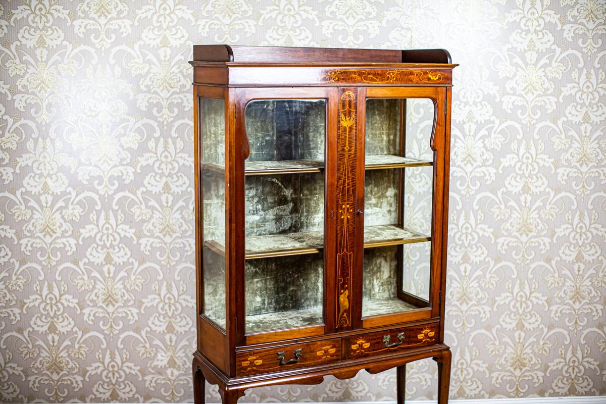 English Mahogany Inlaid Showcase from the 19th Century

A piece of furniture made of mahogany wood, dating back to the 2nd half of the 19th century. It consists of a base on tall legs, connected by a shelf, and a two-winged display with drawers at