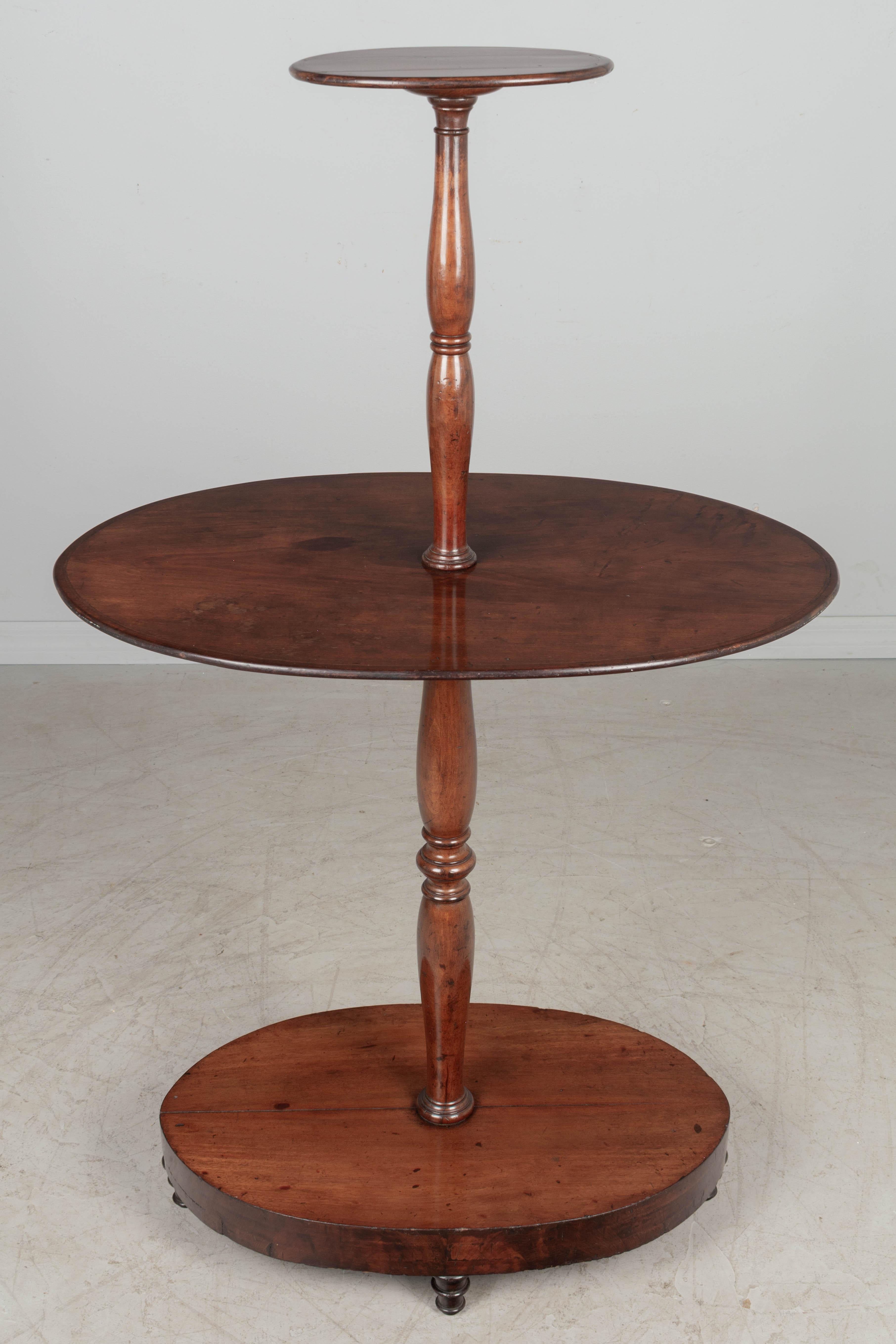A late 19th century English mahogany oval tiered dumbwaiter or dessert server, with turned center pole. Oval base with mahogany veneer and turned feet. This table will be dismantled for shipping via white glove delivery. Circa 1880-1900. 
Overall