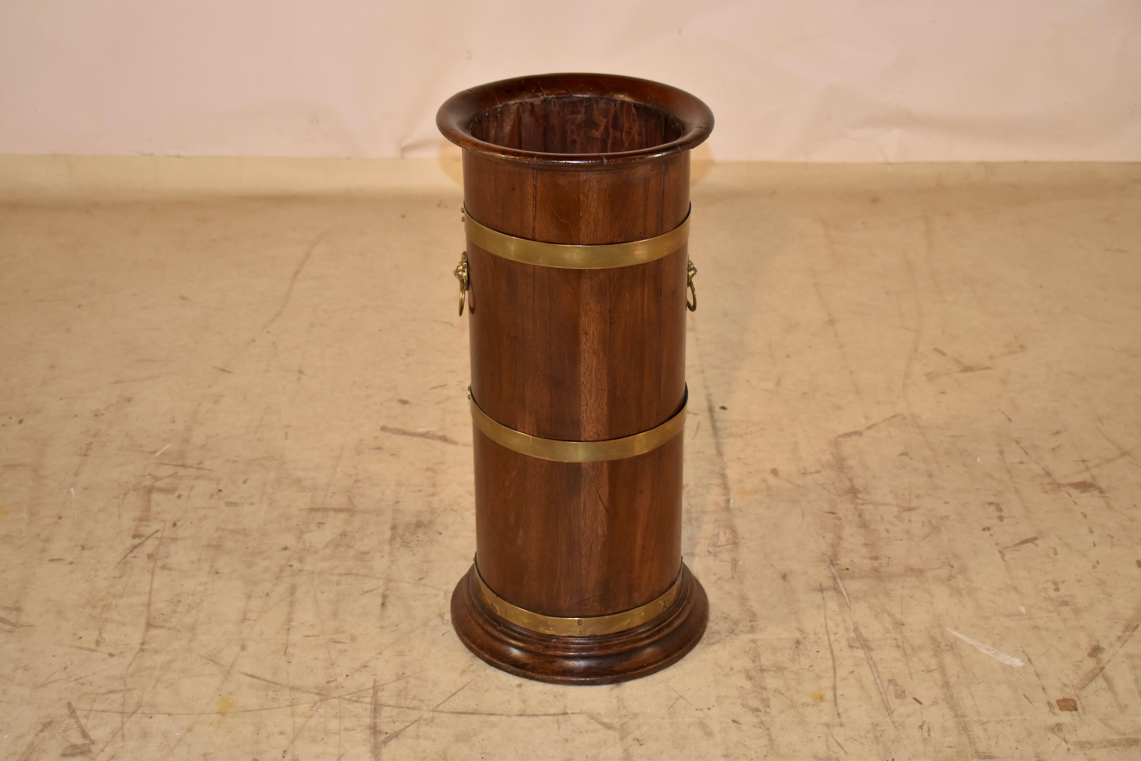 19th century mahogany umbrella or cane stand from England.  The rim and the base are turned and the stand is made up of mahogany slats, banded together with brass straps.  The sides are decorated with lion's heads handles.  This is an absolutely