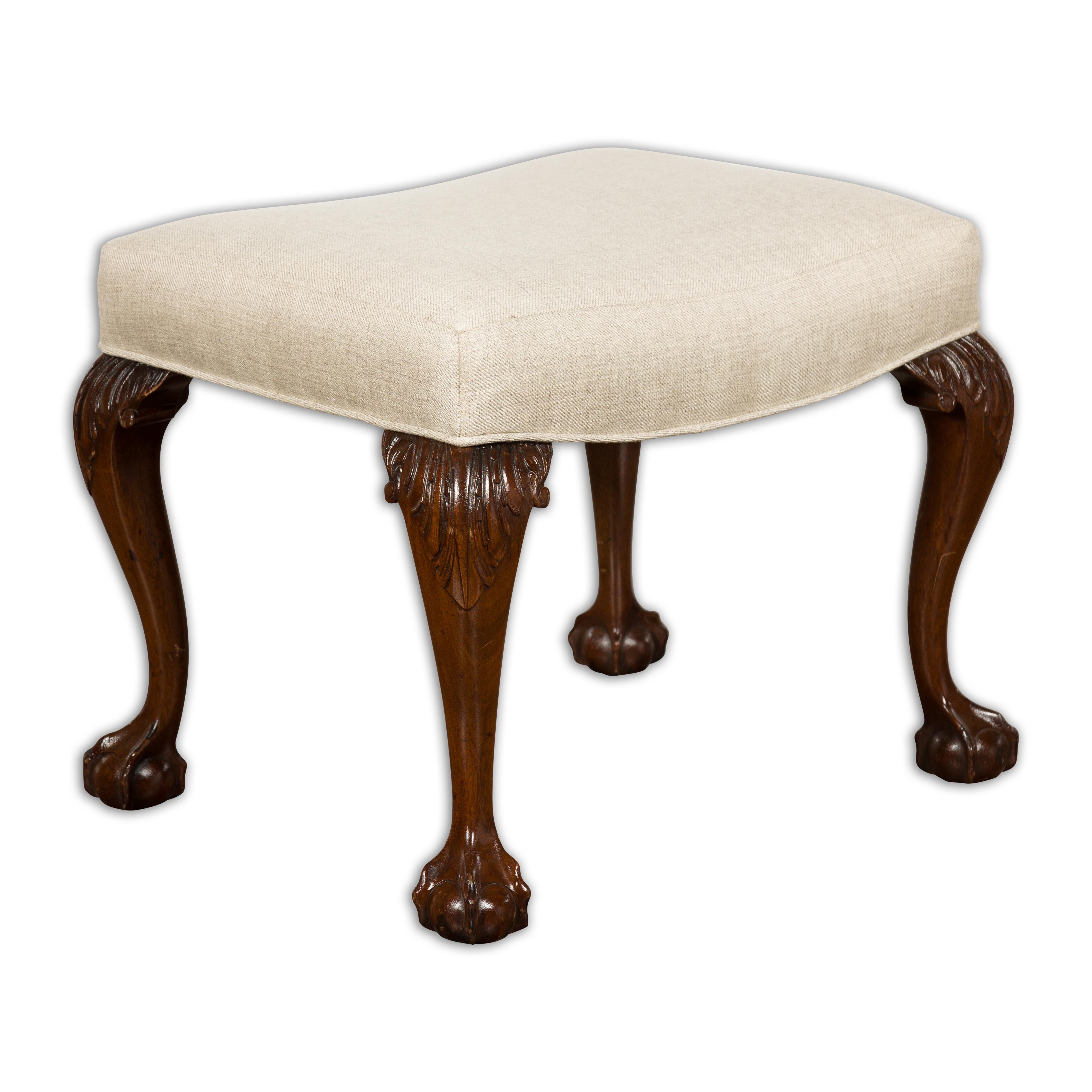 An English mahogany stool from the 19th century with cabriole legs, ball and claw feet and new custom linen upholstery. Exuding an air of stately English elegance, this 19th-century mahogany stool captures the essence of refined craftsmanship and