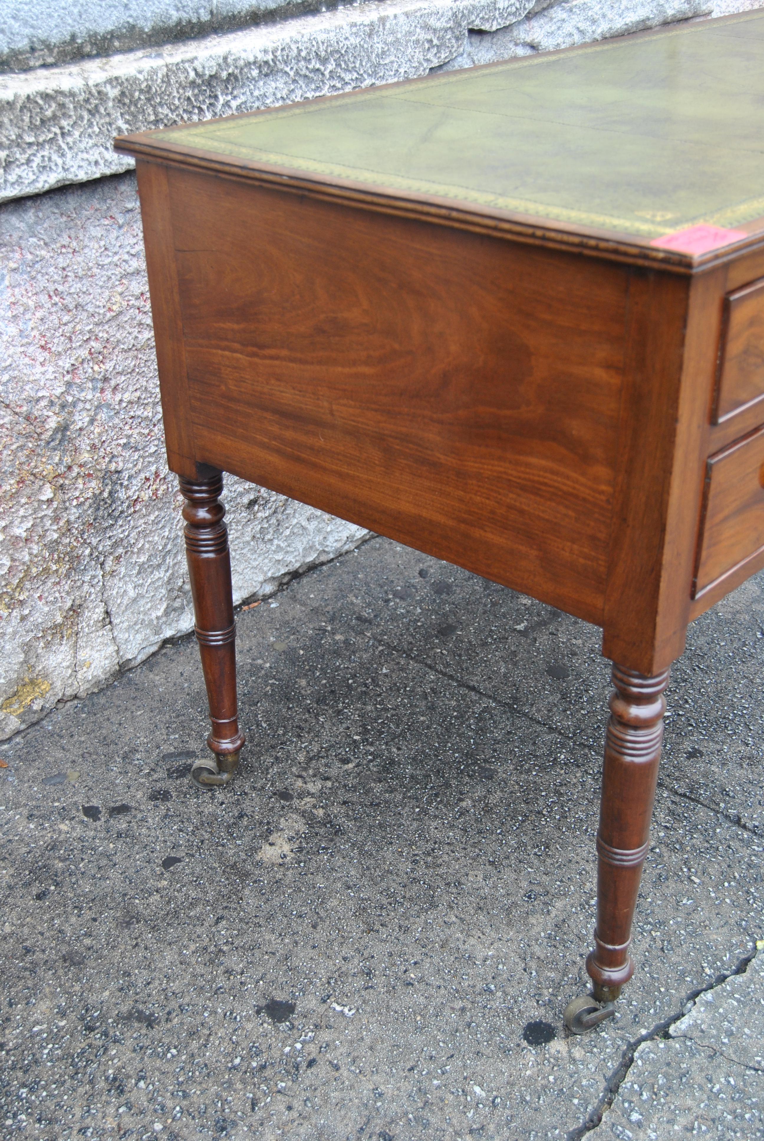 This is a mahogany writing table / desk made in England, circa 1870. The top of the desk has a very nice green leather writing surface with gold gilt tooling. The front edge and the right and left edges of the top are reeded. There are 2 drawers on