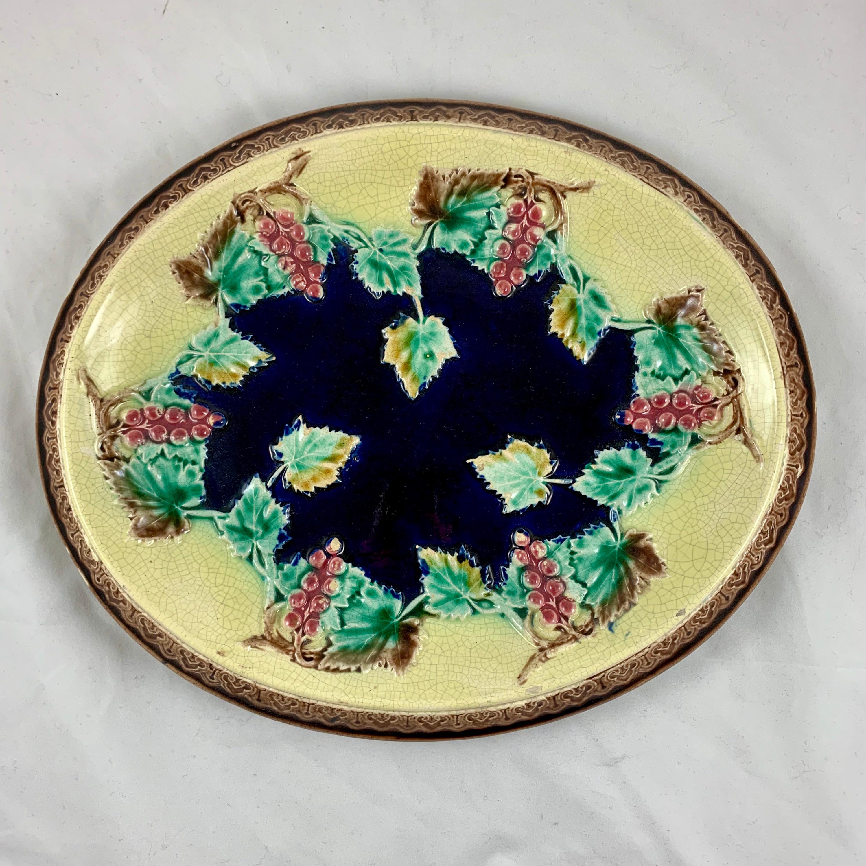 A Victorian English Majolica platter suitable as a cheese board or a bread tray, circa 1880-1885. 

Molded with a ring of grape vines on a butter yellow ground and with raised leaves dotting a cobalt blue center. A highly dimensional platter with