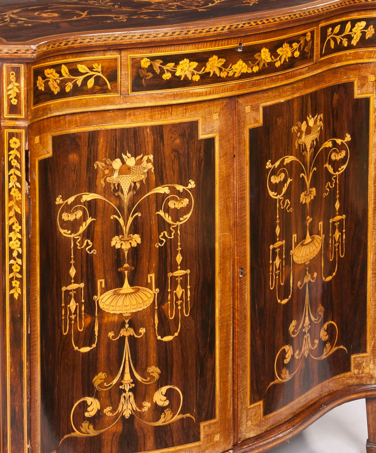 A Fine and Decorative Side Cabinet in the Hepplewhite Manner

Constructed in goncalo alves, with satinwood crossbanding and specimen woods used in the inlays; of serpentine form, rising from spade footed tapered legs, the swept ends framing the two