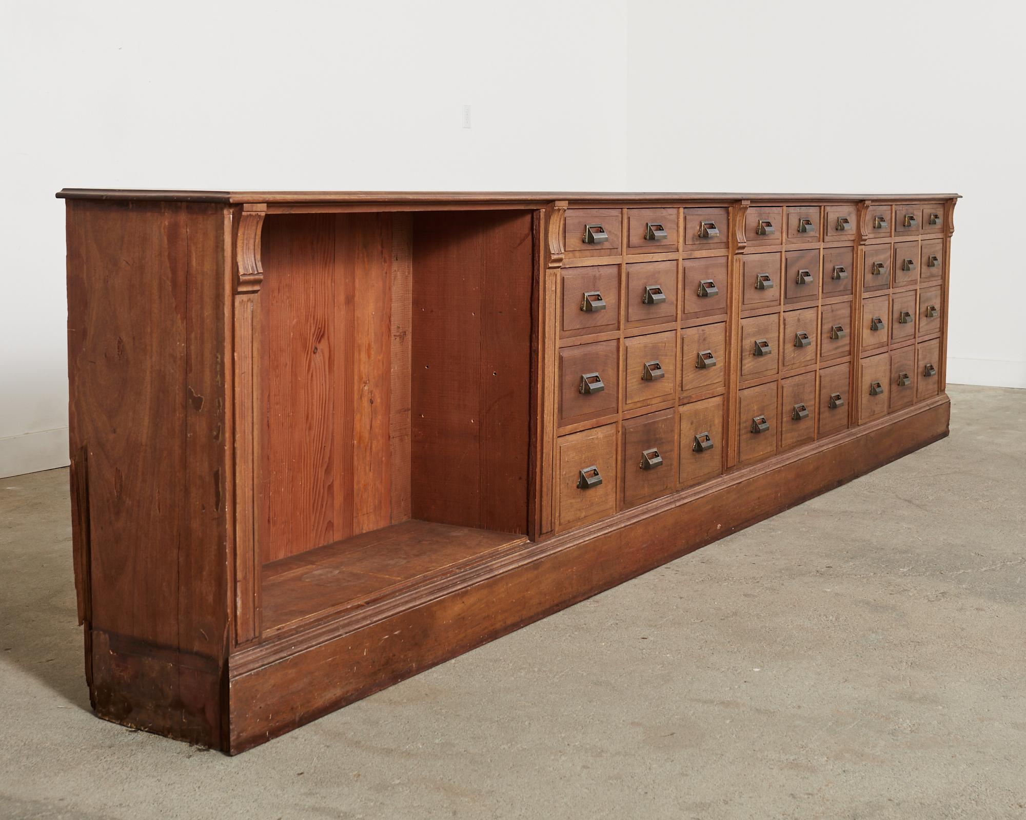 Grand late 19th/early 20th century apothecary cabinet chest of drawers featuring 36 storage drawers with patinated brass pulls. The monumental cabinet measures over 15 feet long and is purported to be from a haberdashery in England then used in an