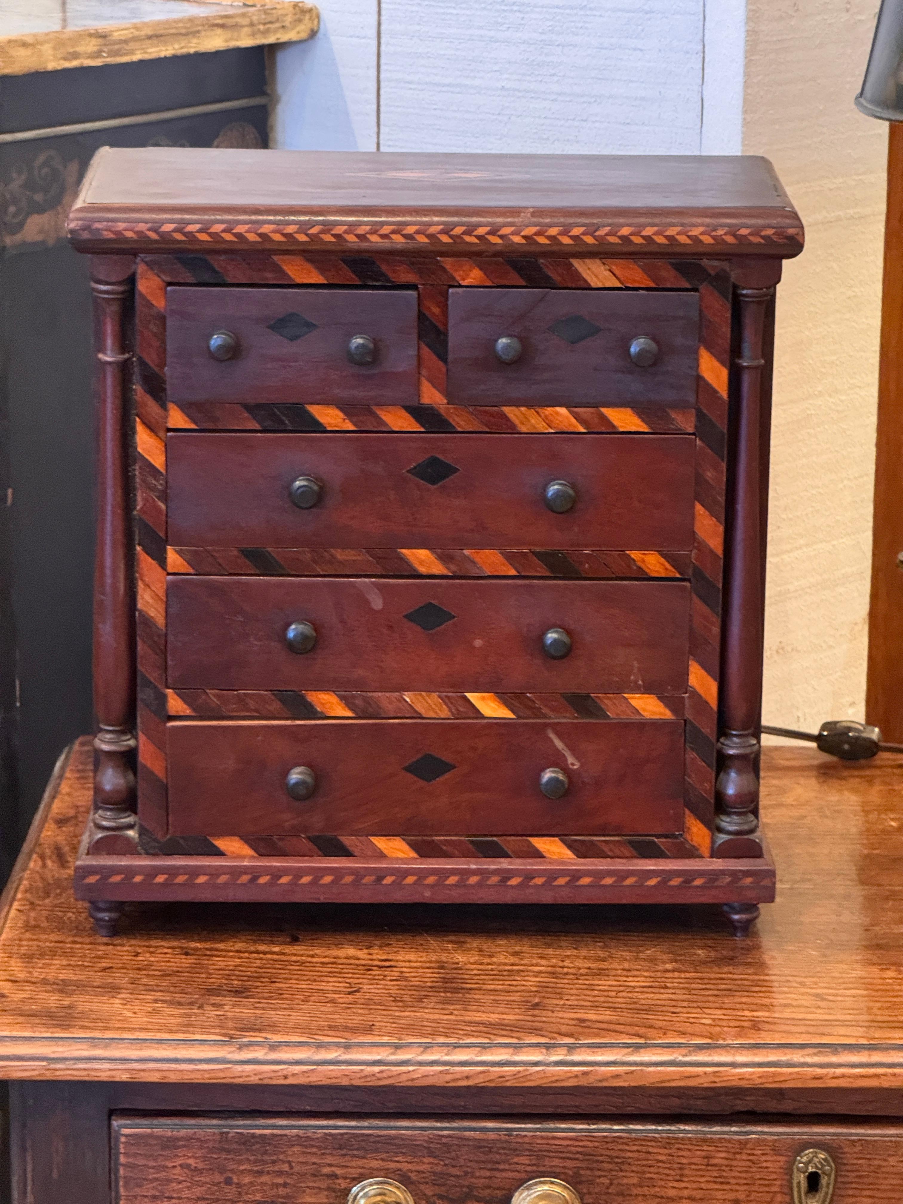 Cassettone inglese del XIX secolo con cinque cassetti e intarsio geometrico lungo la parte anteriore. Le colonne laterali tornite fiancheggiano la cassa e la base intarsiata è un pezzo separato e rimovibile, mostrato nell'immagine di dettaglio.