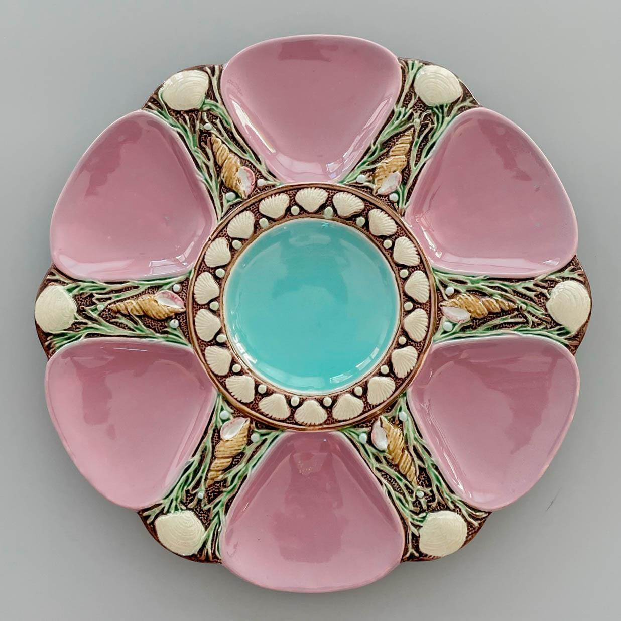 A 19th Century English Minton Majolica oyster plate, with an aqua blue center well and six mauve pink oyster wells separated by seashells, scallops and green seaweed in relief on brown ground. Green glazed underside with Minton stamp. There is an