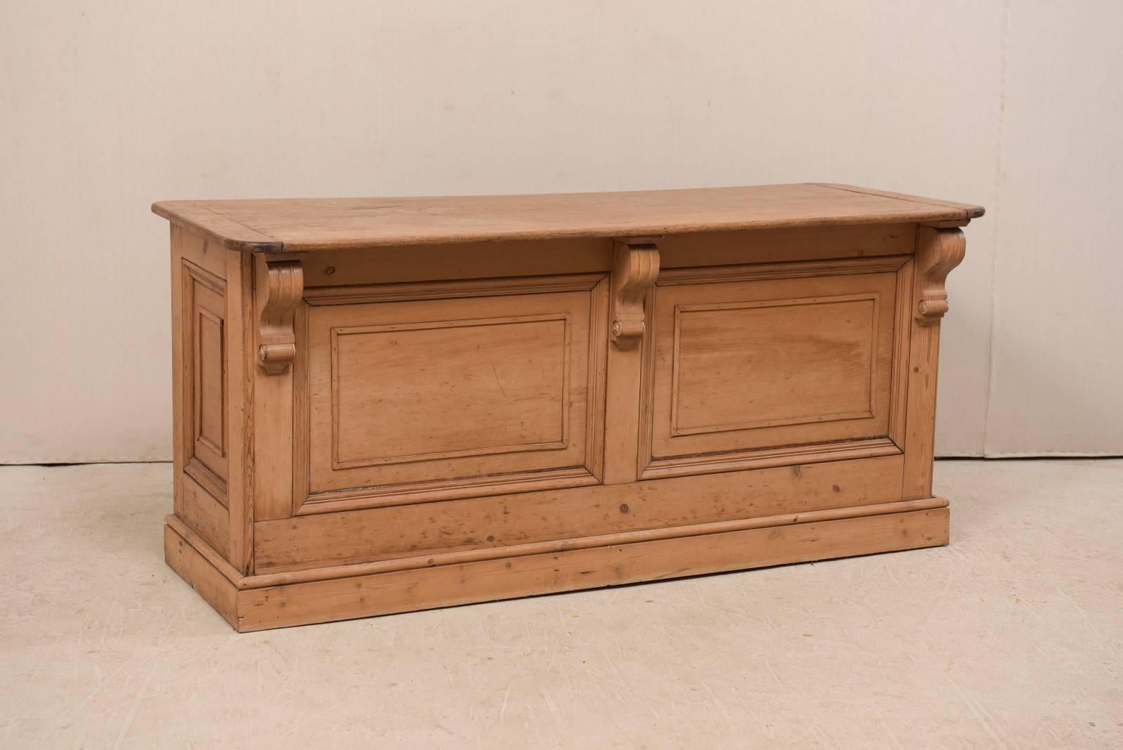An English kitchen island from the 19th century. This antique natural finished wooden island features a rectangular-shaped overhanging top (at one long side) supported with three large carved volute brackets, with recessed panels decorating the