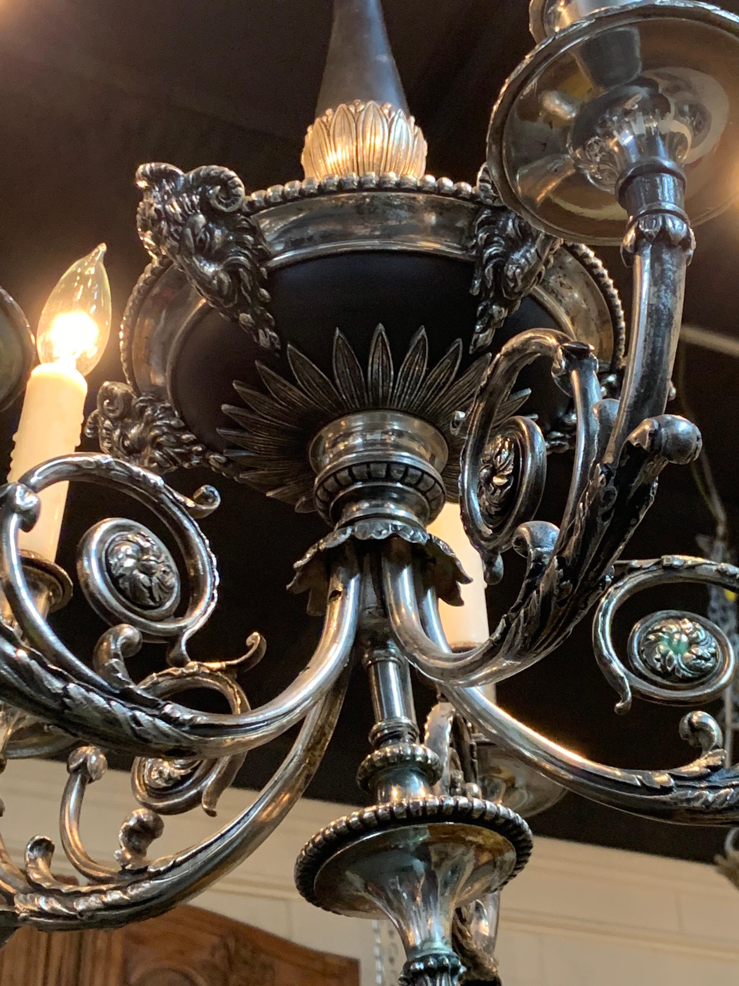 Elégant lustre à tole de style néoclassique du 19ème siècle, argenté sur bronze. Beaux détails décoratifs, notamment des têtes de béliers sur la base. Très unique !