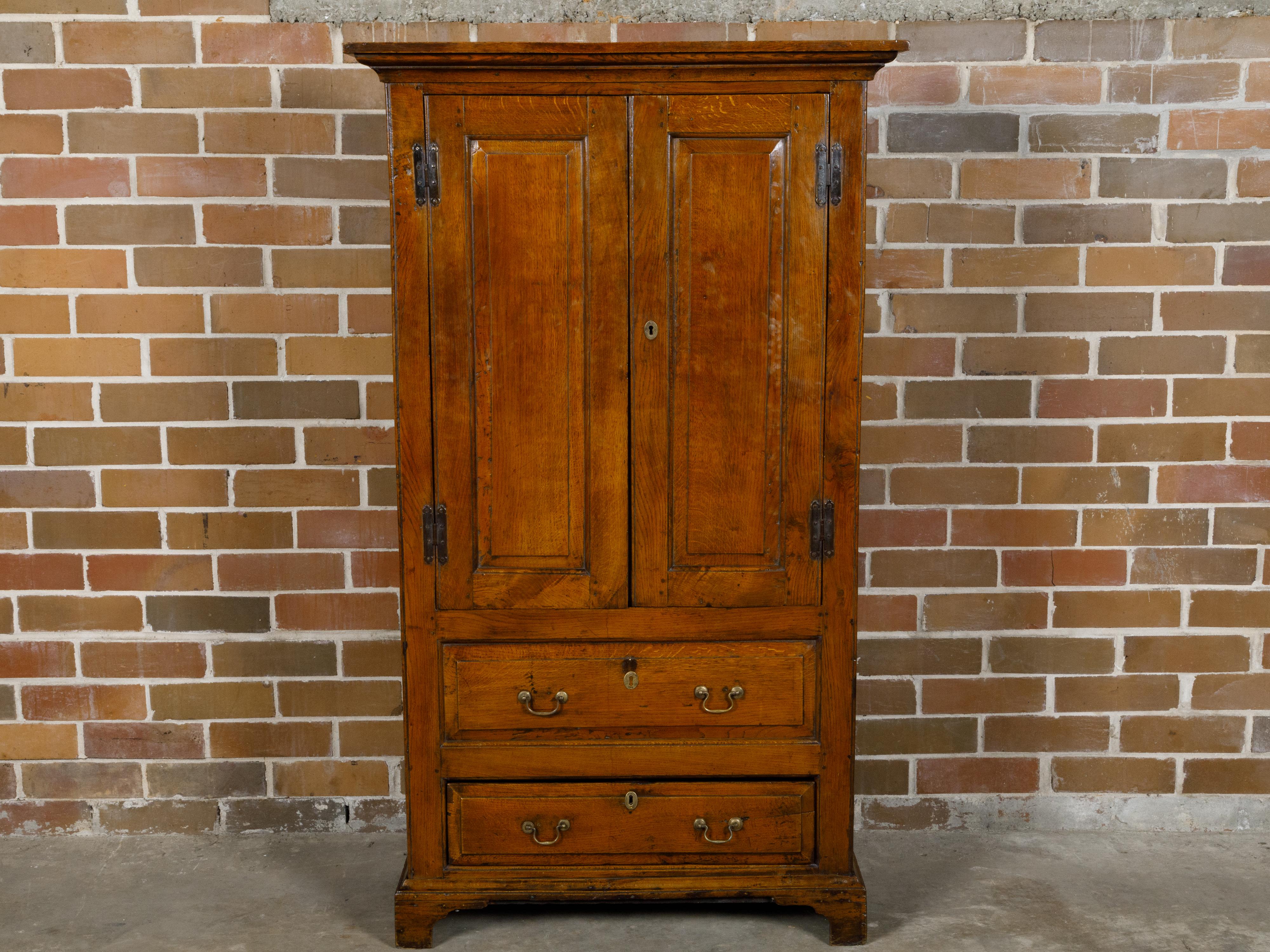 An English oak armoire from the 19th century with two doors over two drawers and bracket feet. This oak armoire, featuring two doors over two drawers and resting on sturdy bracket feet, is a testament to the durability and timeless appeal of classic