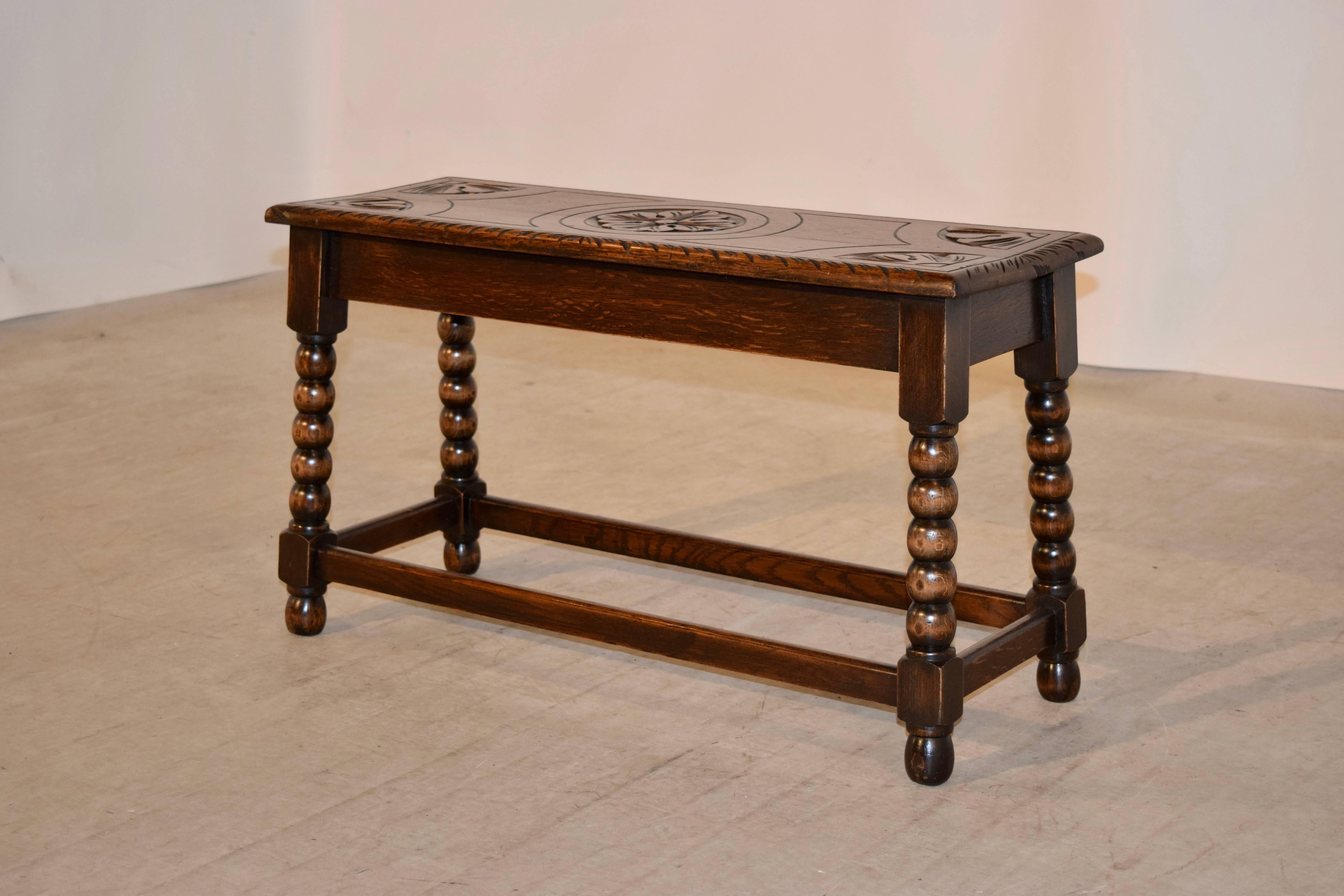 19th century English oak bench with a carved decorated top and follows down to a simple apron and supported on hand-turned legs, which are splayed and joined by simple stretchers. The bench is raised on hand-turned feet.