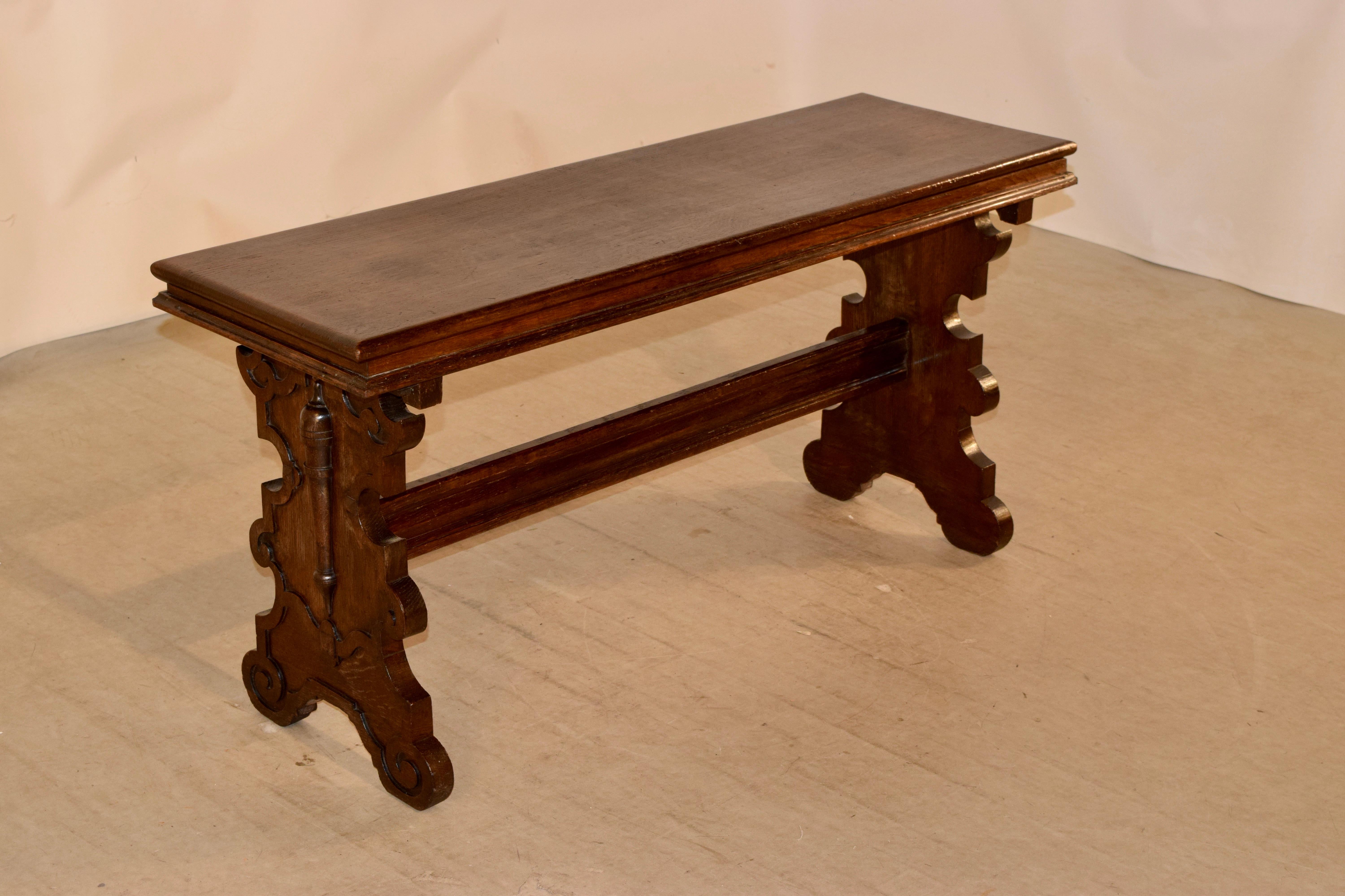 19th century oak bench from England in the Renaissance style. The seat is a single plank with a molded edge surround, following down to trestle legs with lovely scalloped and carved designs joined by a nice stretcher.