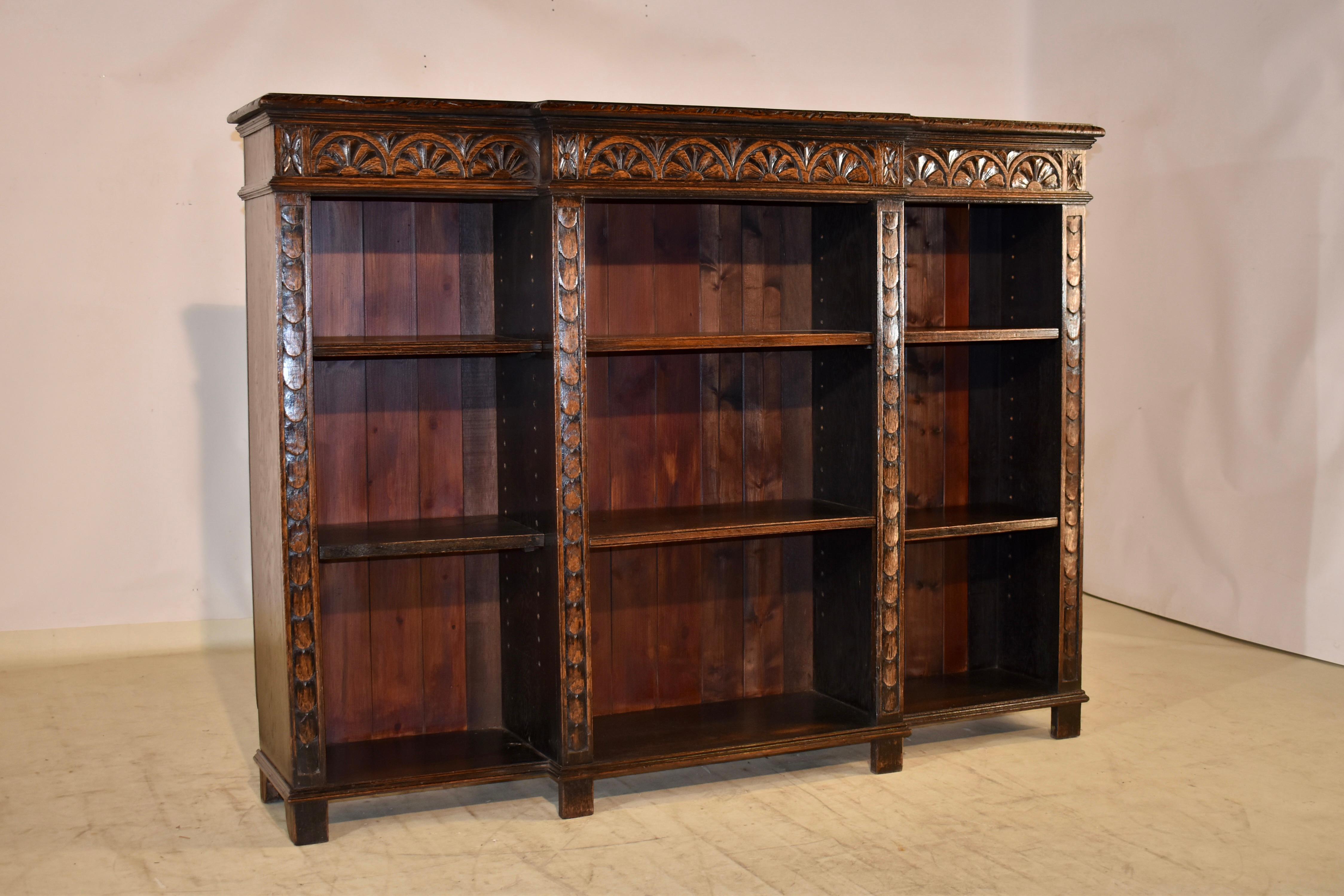 19th century oak breakfront bookcase from England.  The top is made from a single board, and has a beveled and hand carved decorated edge, following down to simple sides and a hand carved decorated apron over three sections of bookcase, each with