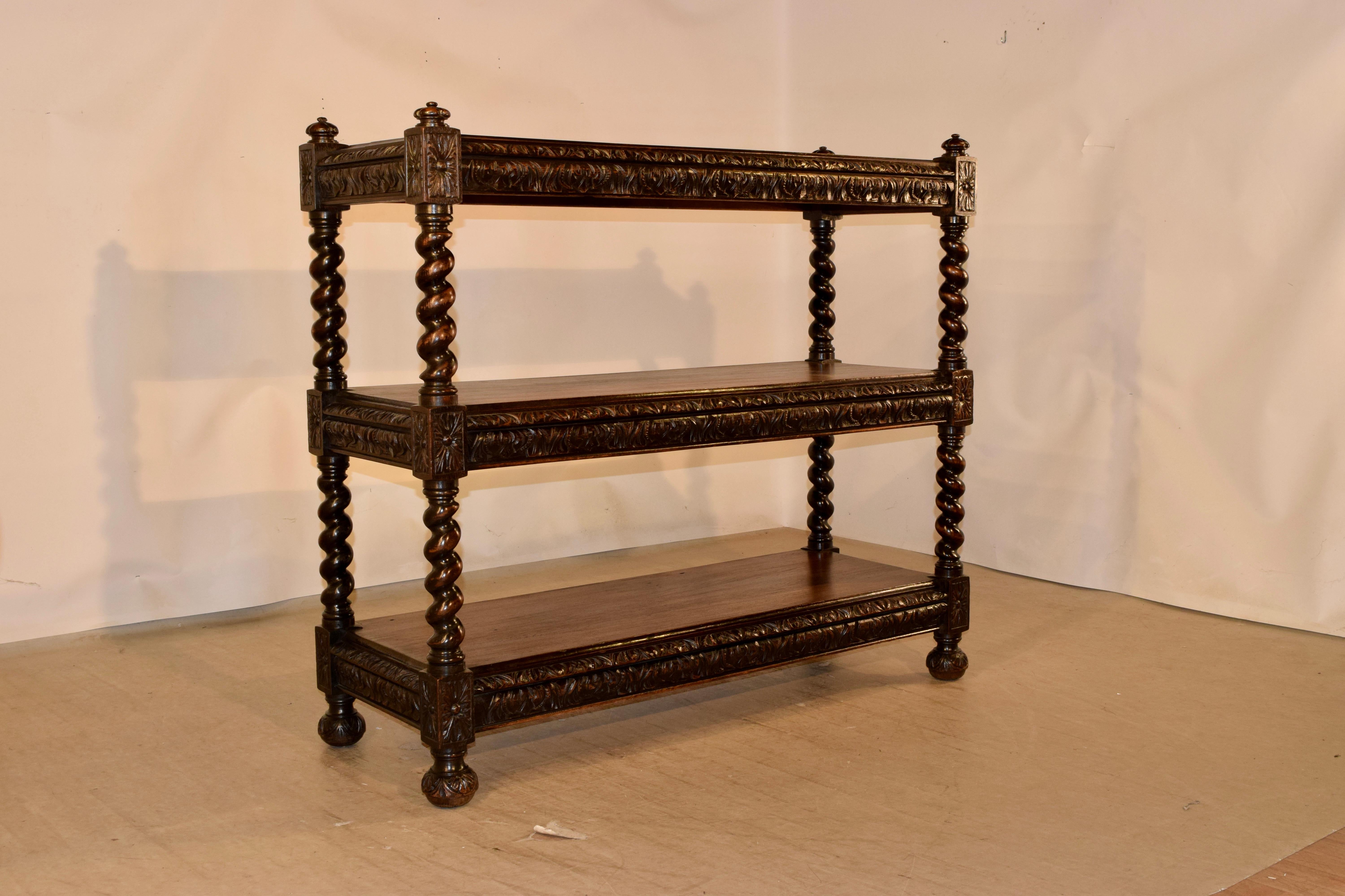 19th century English oak buffet with four hand turned and carved finials at the top over three shelves, all with hand carved and beveled edges over three hand carved aprons, all separated by hand turned barley twist shelf supports. The piece is