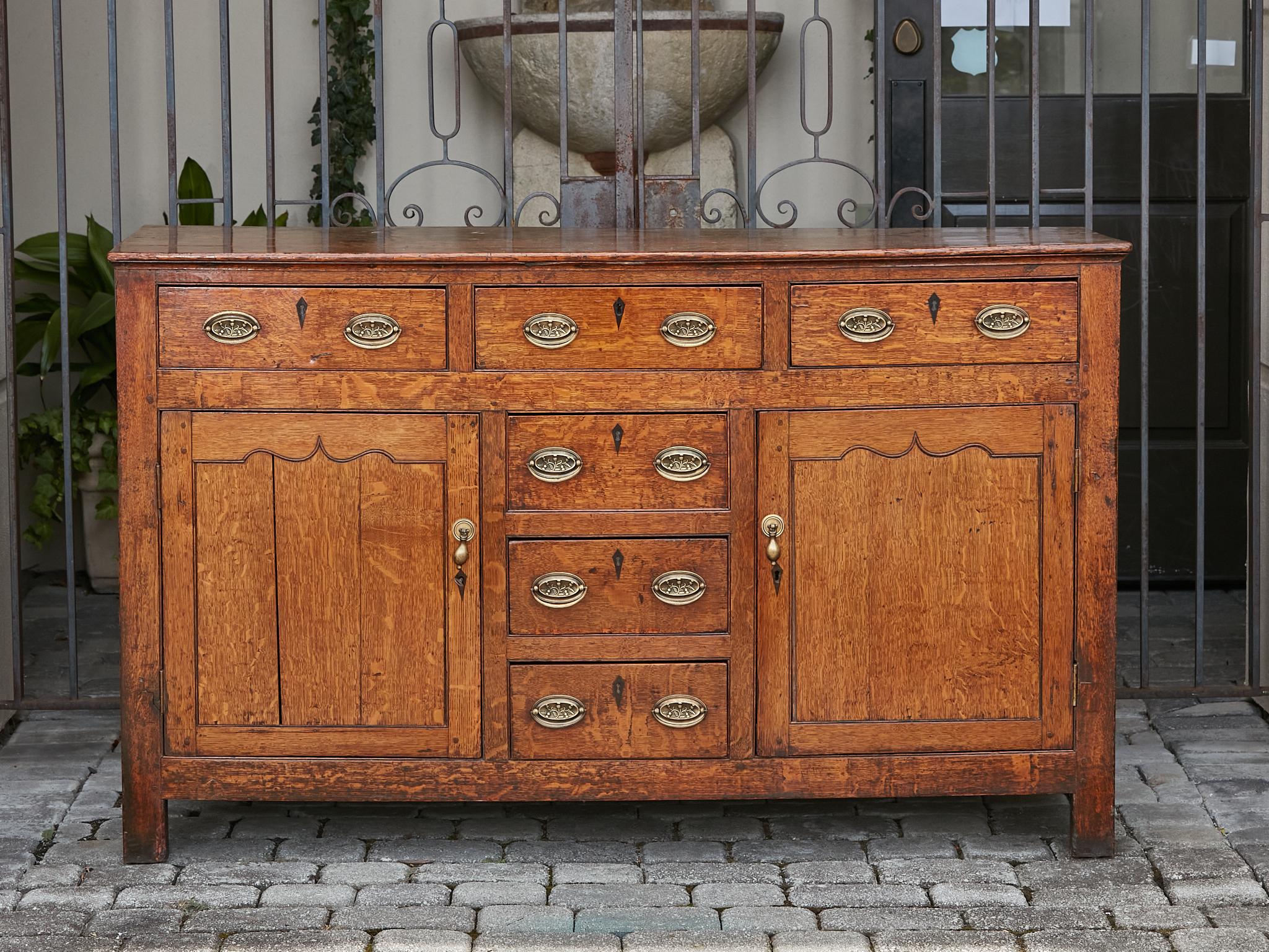 An English oak buffet from the 19th century with six drawers, two doors and brass hardware. This 19th-century English oak buffet is a handsome celebration of craftsmanship and practical design. Showcasing a warm, rich oak hue, the buffet is