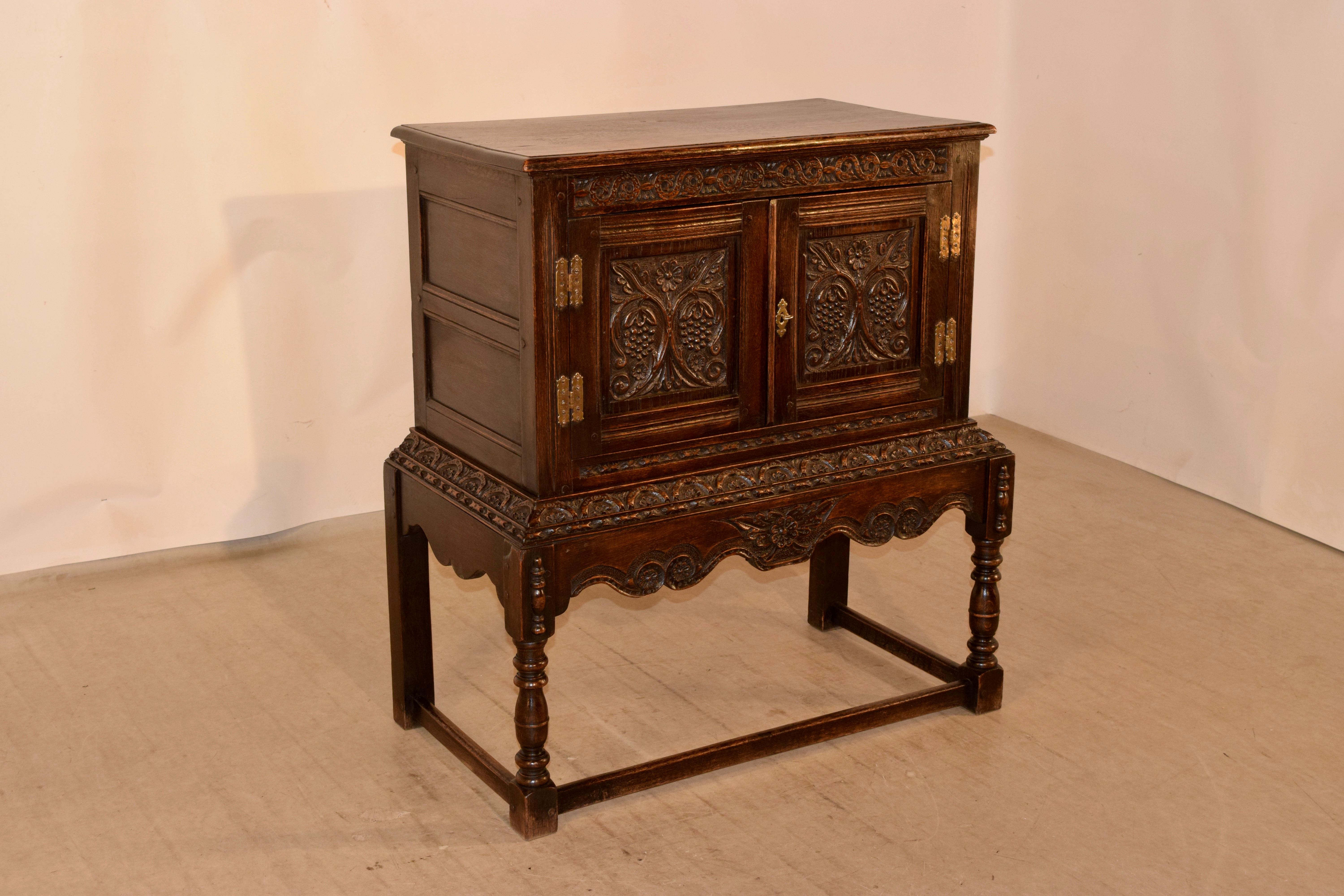 19th century oak cabinet on stand from England with a beveled edge around the top following down to hand paneled sides and a spectacularly hand carved decorated frieze over two paneled doors, which also have carved decorated panels over a lovely