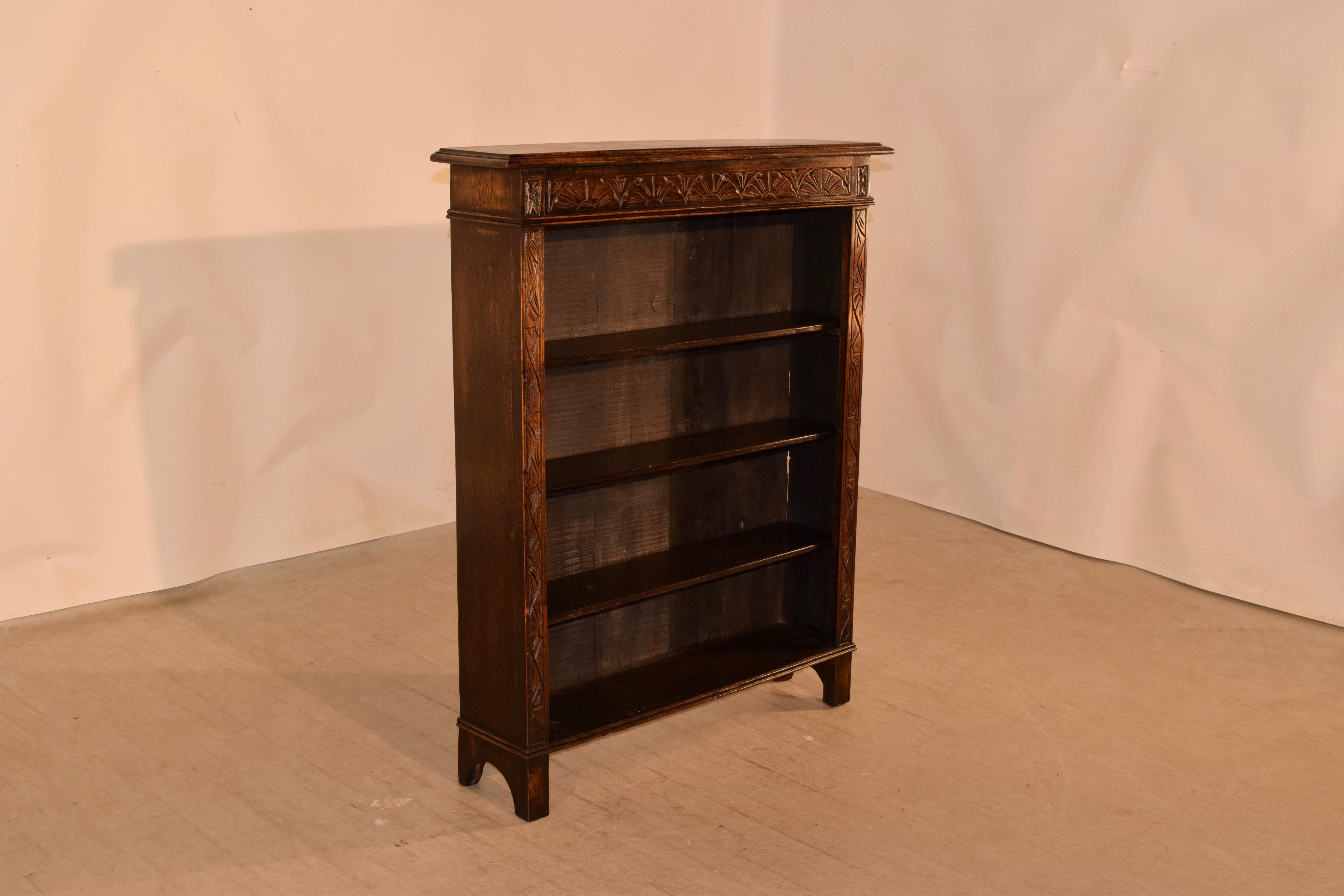 19th century oak bookcase from England with a beveled edge around the top. This follows down to a four shelves flanked by hand carved decorated face of the case and simple sides. The case is raised on bracket feet.