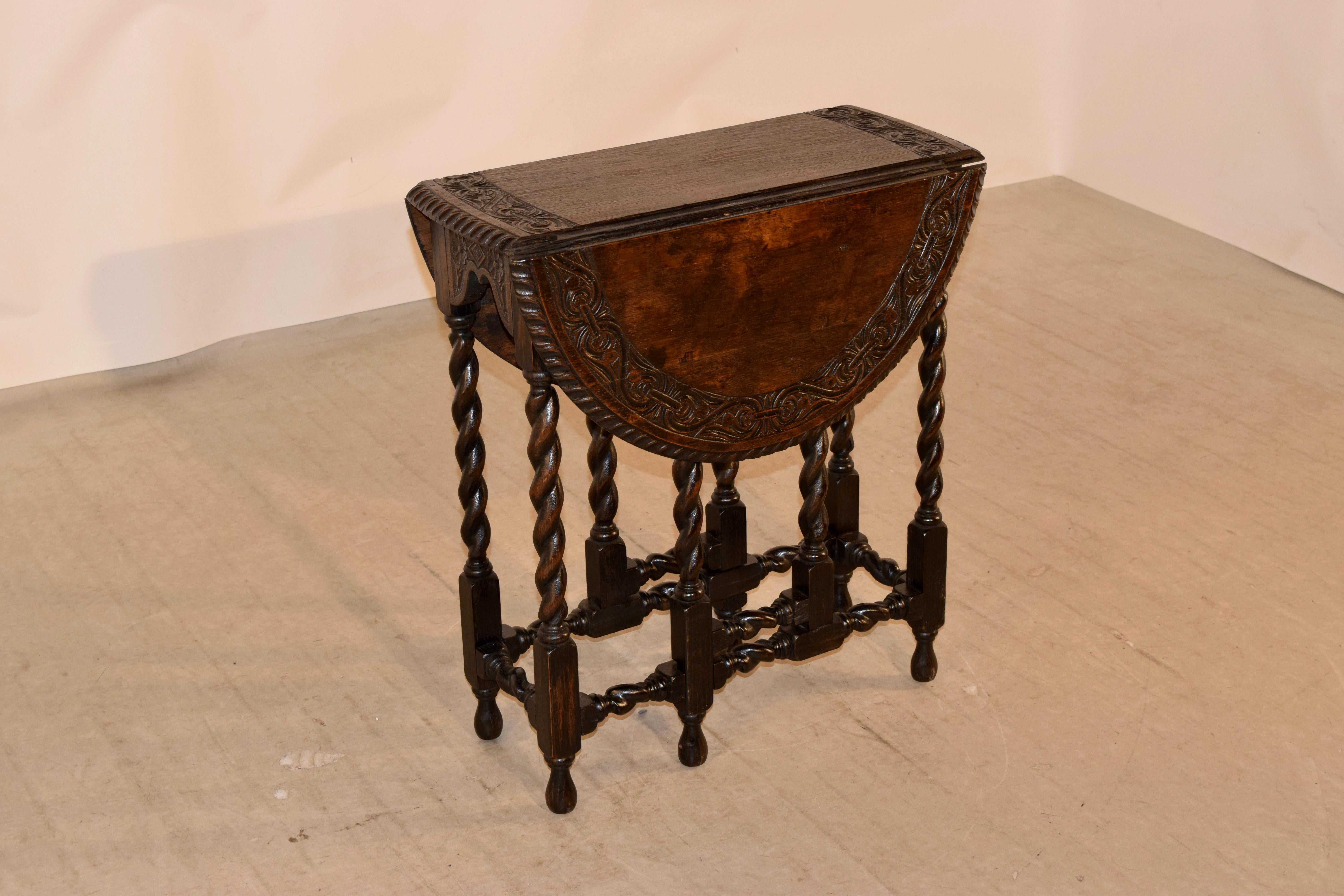 19th century oak gate leg table with a carved border around the top, which is surrounded by a deeply hand carved decorated beveled edge. This follows down to a hand carved and scalloped apron and hand turned barley twist legs and gates, all joined