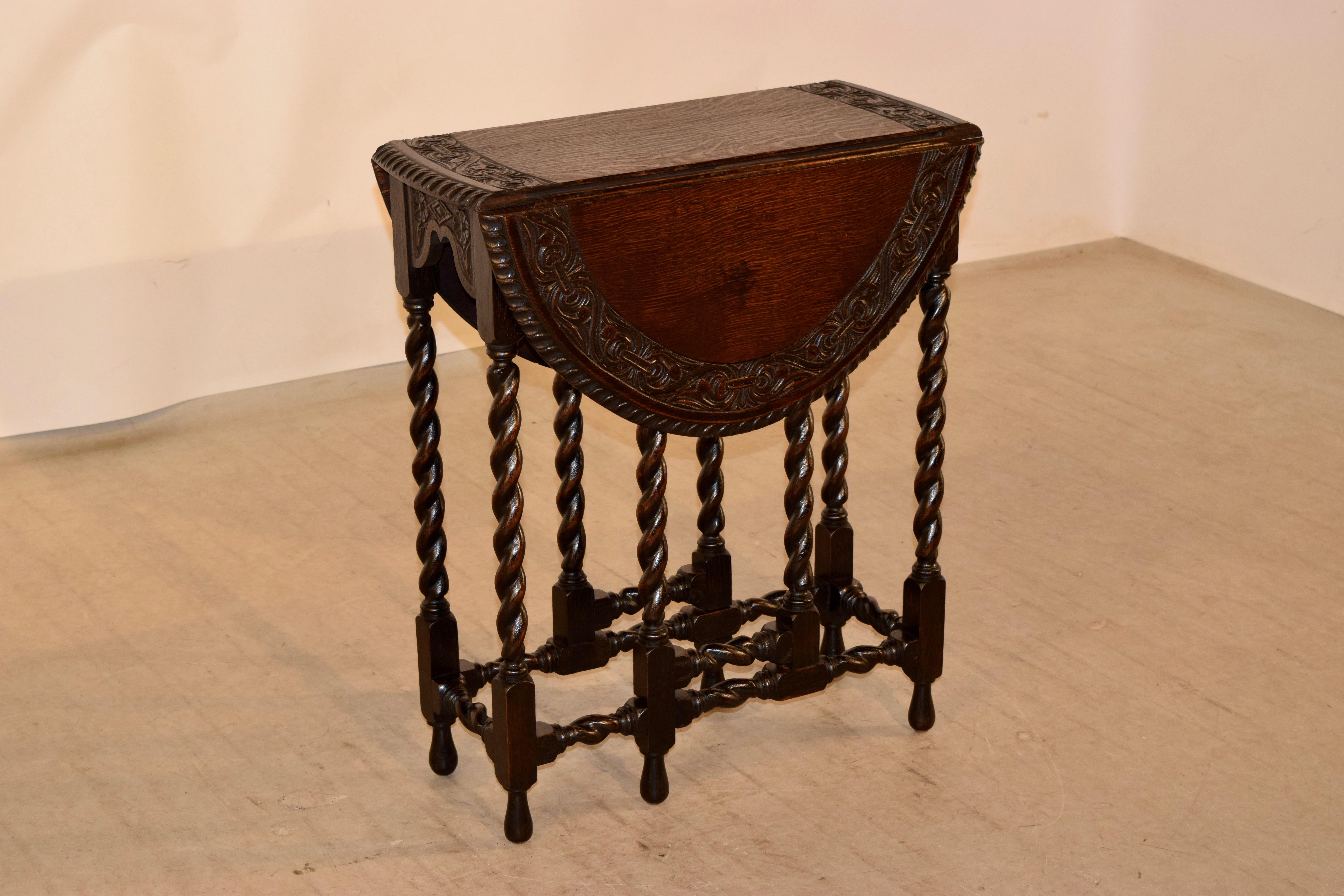 19th century oak gate leg table with a carved border around the top, which is surrounded by a deeply hand carved decorated beveled edge. This follows down to a hand carved and scalloped apron and hand turned barley twist legs and gates, all joined