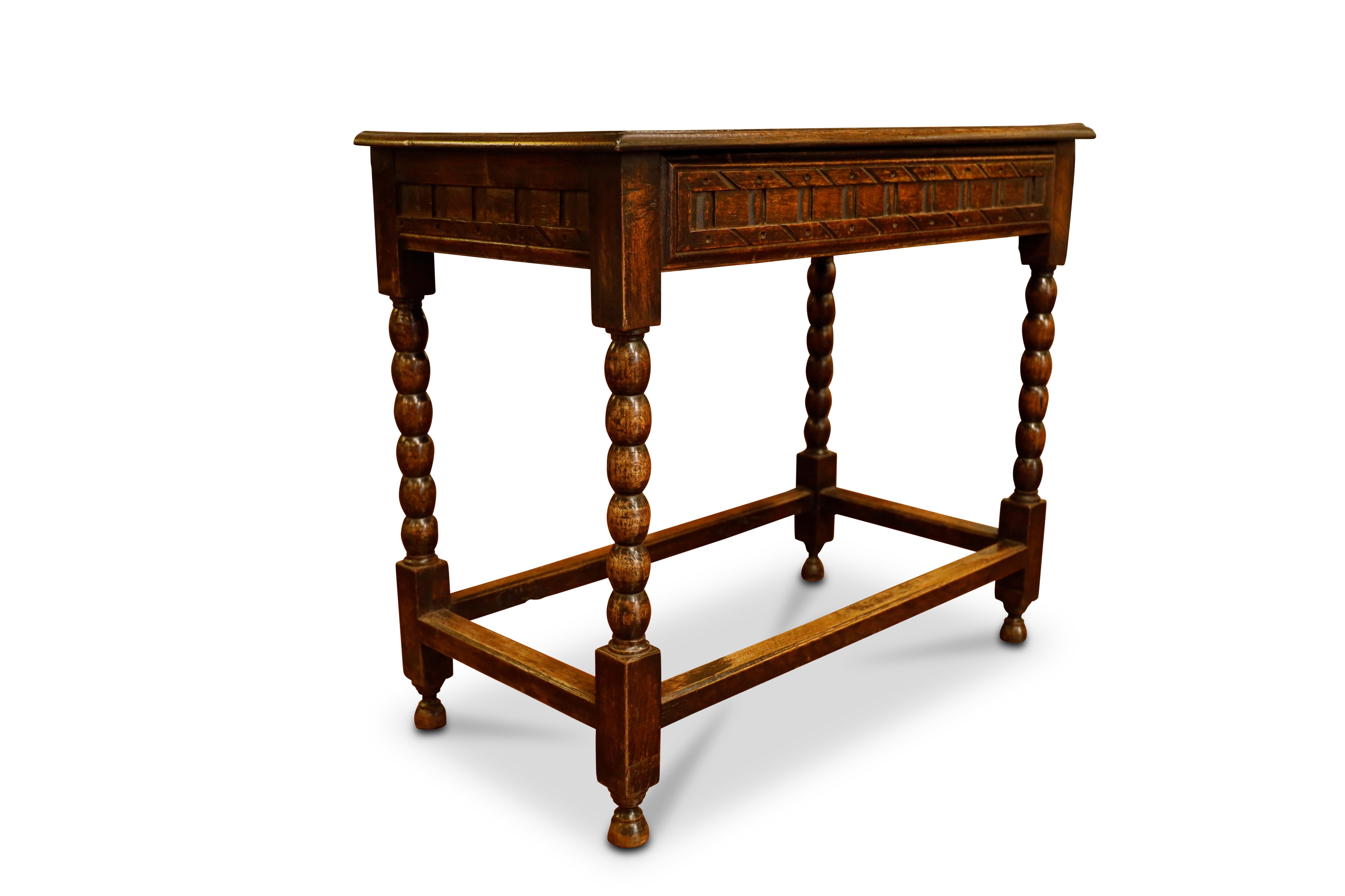 English carved oak writing / side table. Top has peg capped dowels and carved edges.  Single carved front drawer.  Standing on bobbin turned legs ending with bun feet connected by stretchers.