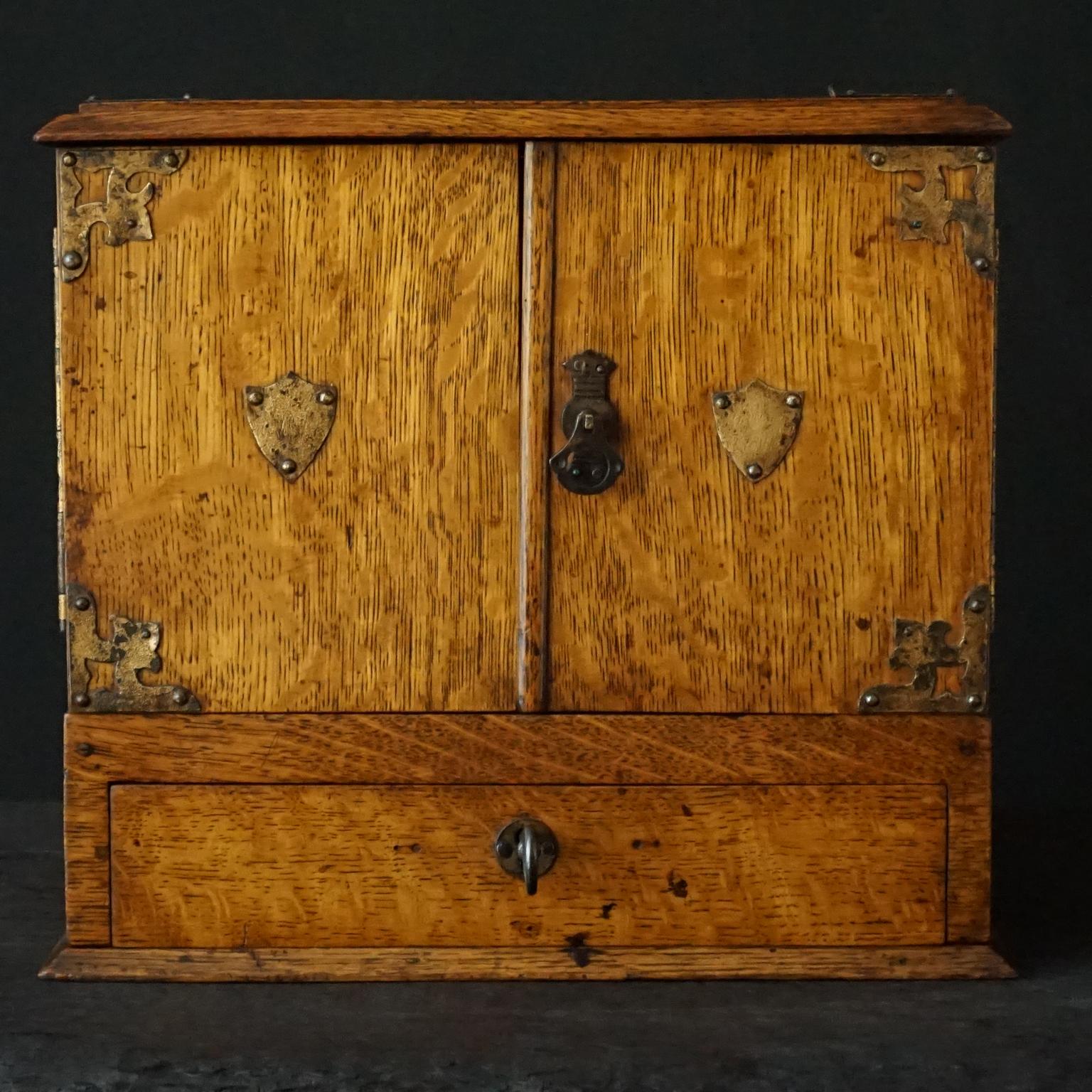 Very decorative pretty late 19th century Victorian oak cigar humidor, shaped as little drawer cabinet with metal decoration.
On the metal shield on the left door it reads a W, on the right I can make out very vaguely some letters (maybe a name?)