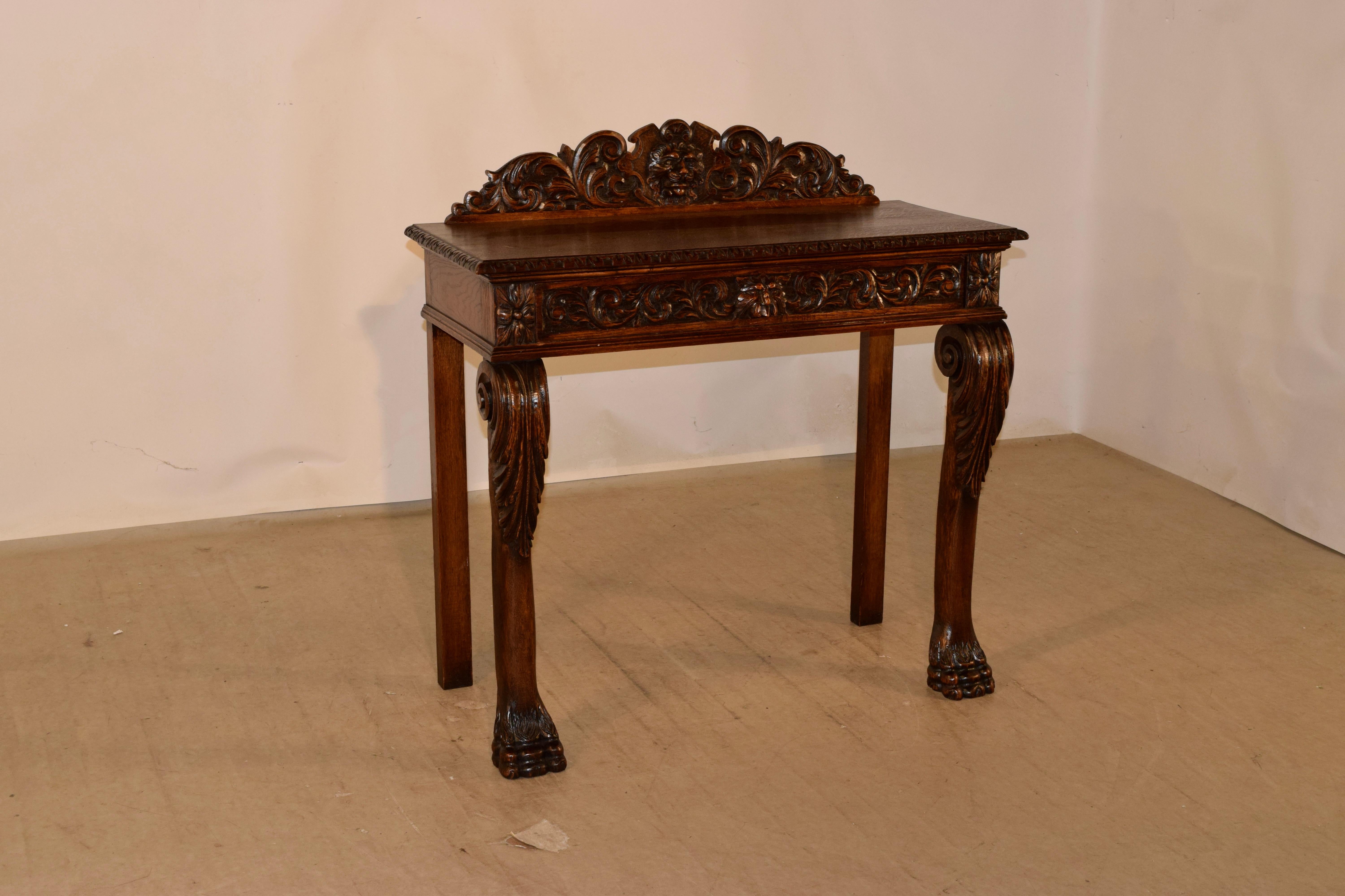 19th century oak console table from England with a stately hand carved decorated backsplash which has a central shield with a lions head surrounded by acanthus leaves, over a top with a beveled and carved decorated edge. This follows down to simple