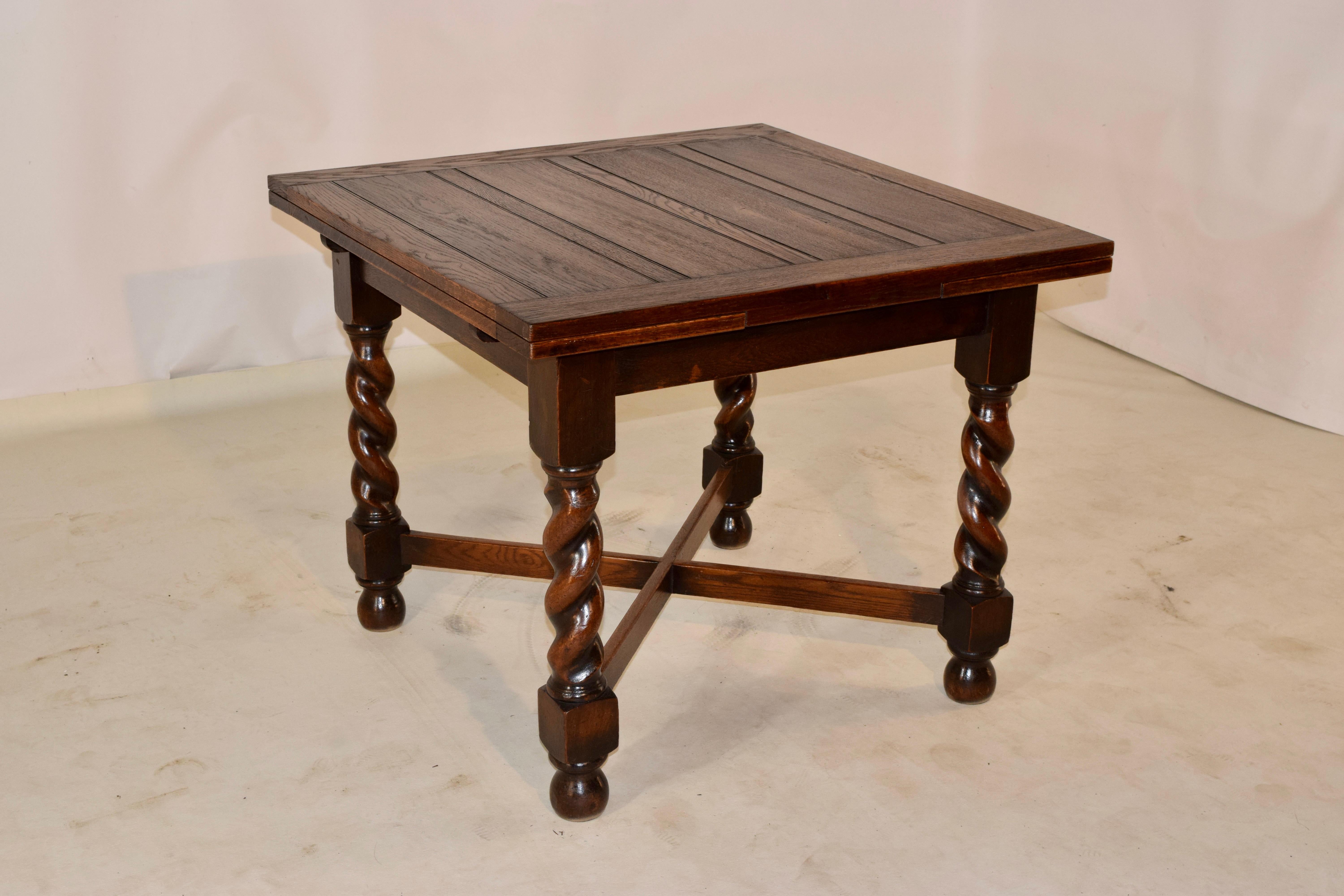 Late 19th century oak table from England with a paneled top and two leaves which draw out from the sides and tuck back in for easy storage. The table has a simple apron and is supported on hand turned barley twist legs, joined by cross stretchers