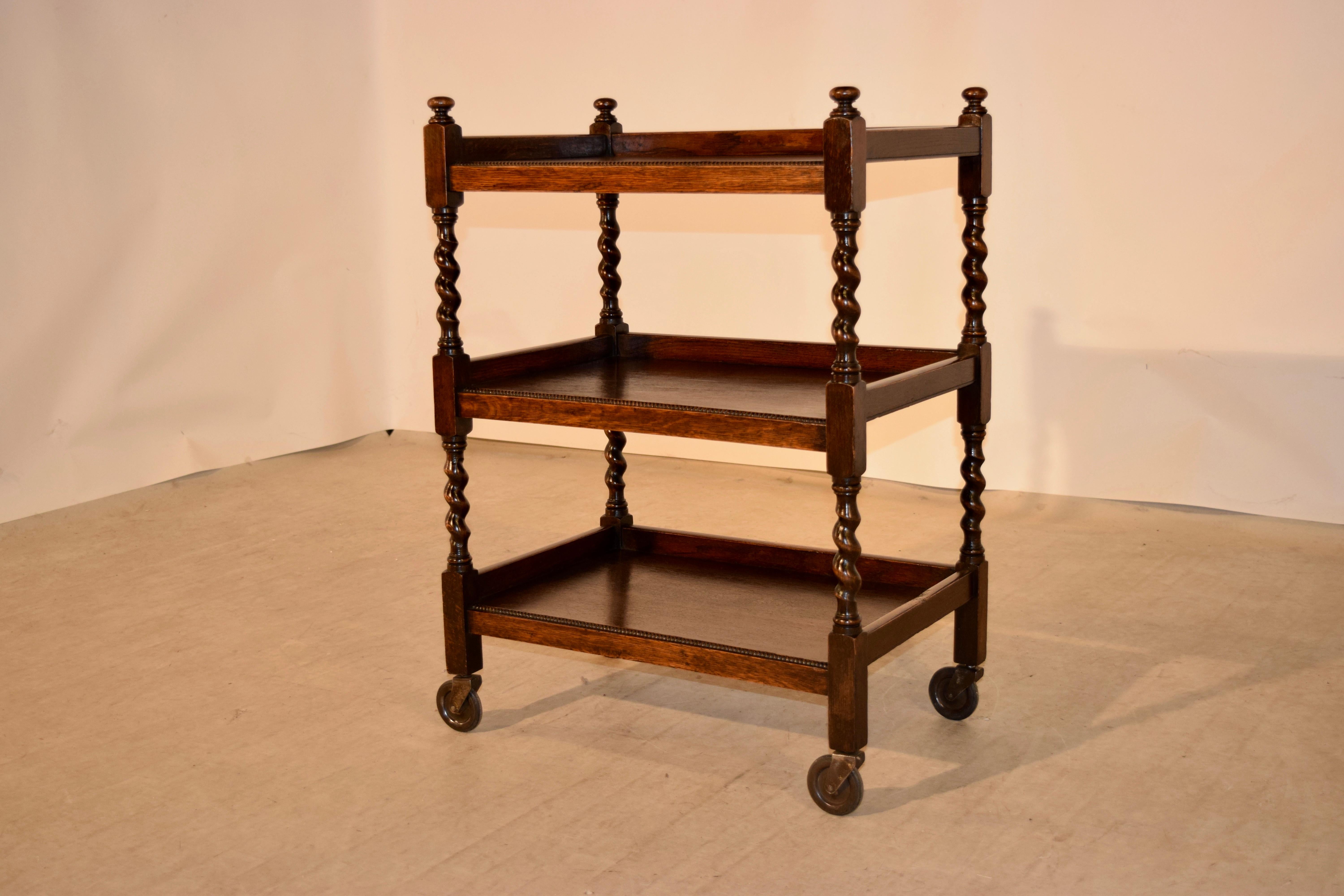19th century oak drinks cart from England. The cart has three shelves with beaded front edges separated by hand-turned barley twist shelf supports and raised on casters.