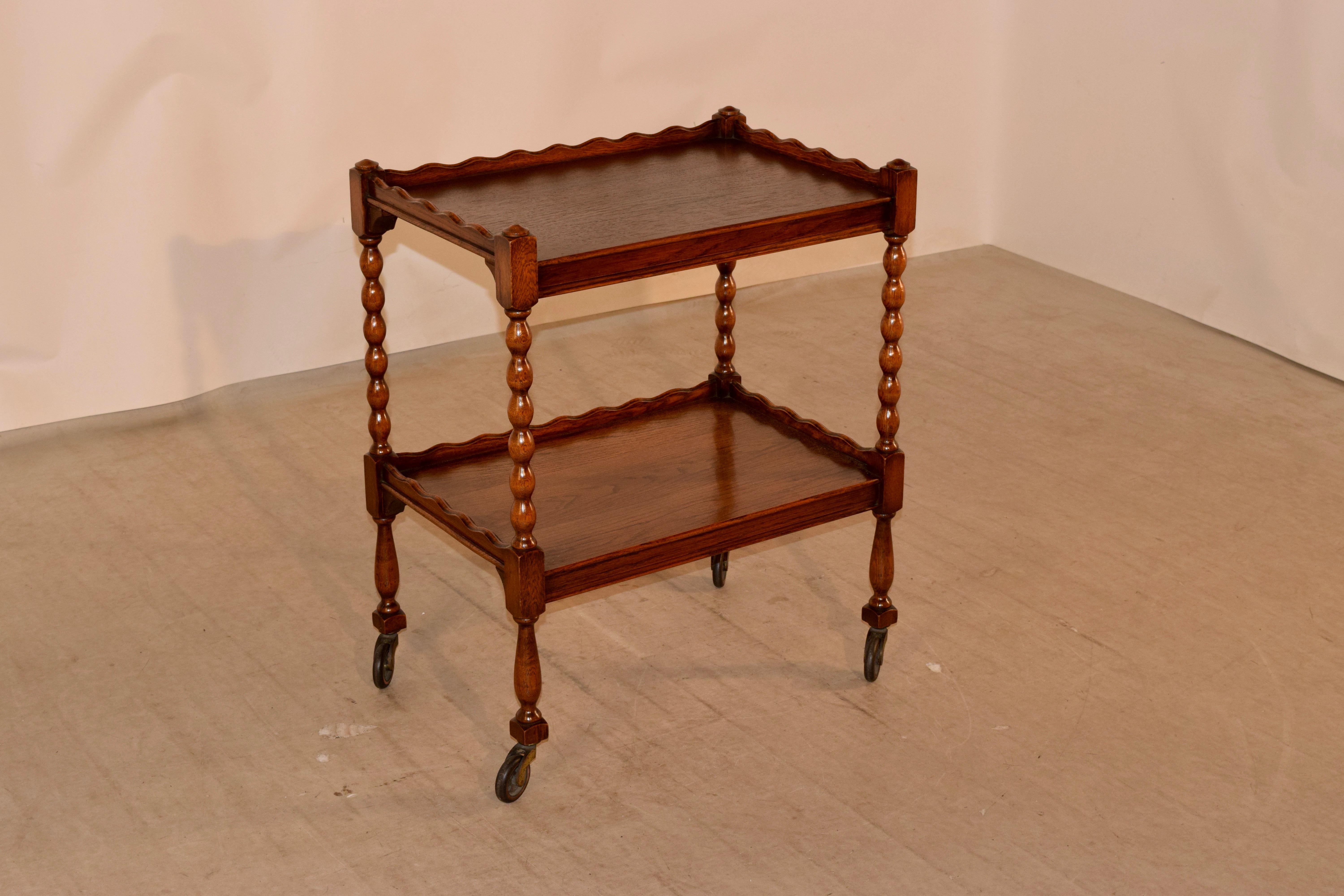 19th century English oak drinks cart with a scalloped gallery around the top following down to a shelf, which is separated from the lower shelf by hand-turned bobbin turned shelf supports. The lower shelf also has a scalloped gallery as well, and