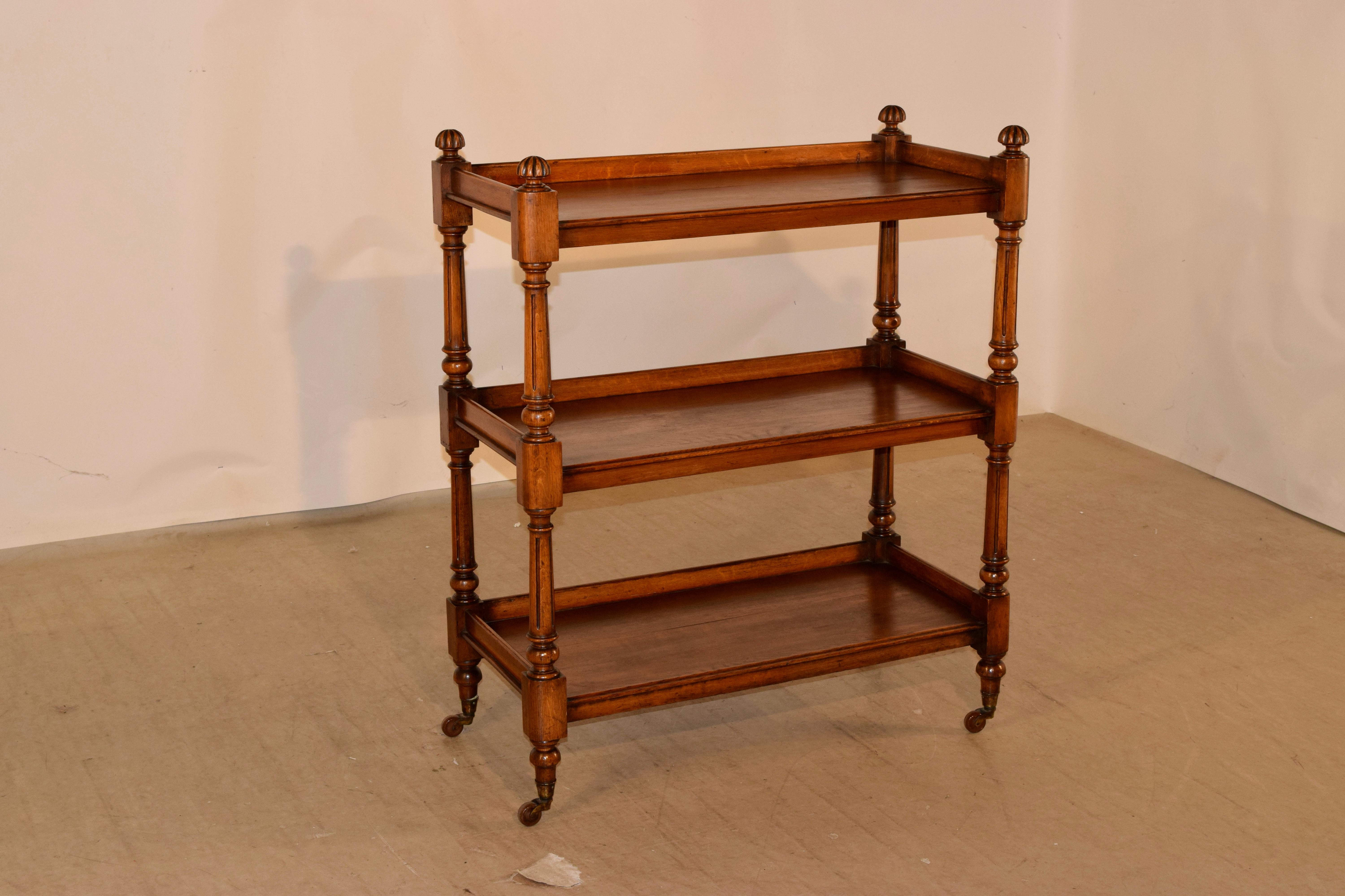 19th century English oak dumbwaiter with finials on the top corners, following down to three shelves with side galleries and molded edges on the fronts. The legs and shelf supports are hand-turned and fluted and are supported on the original casters.