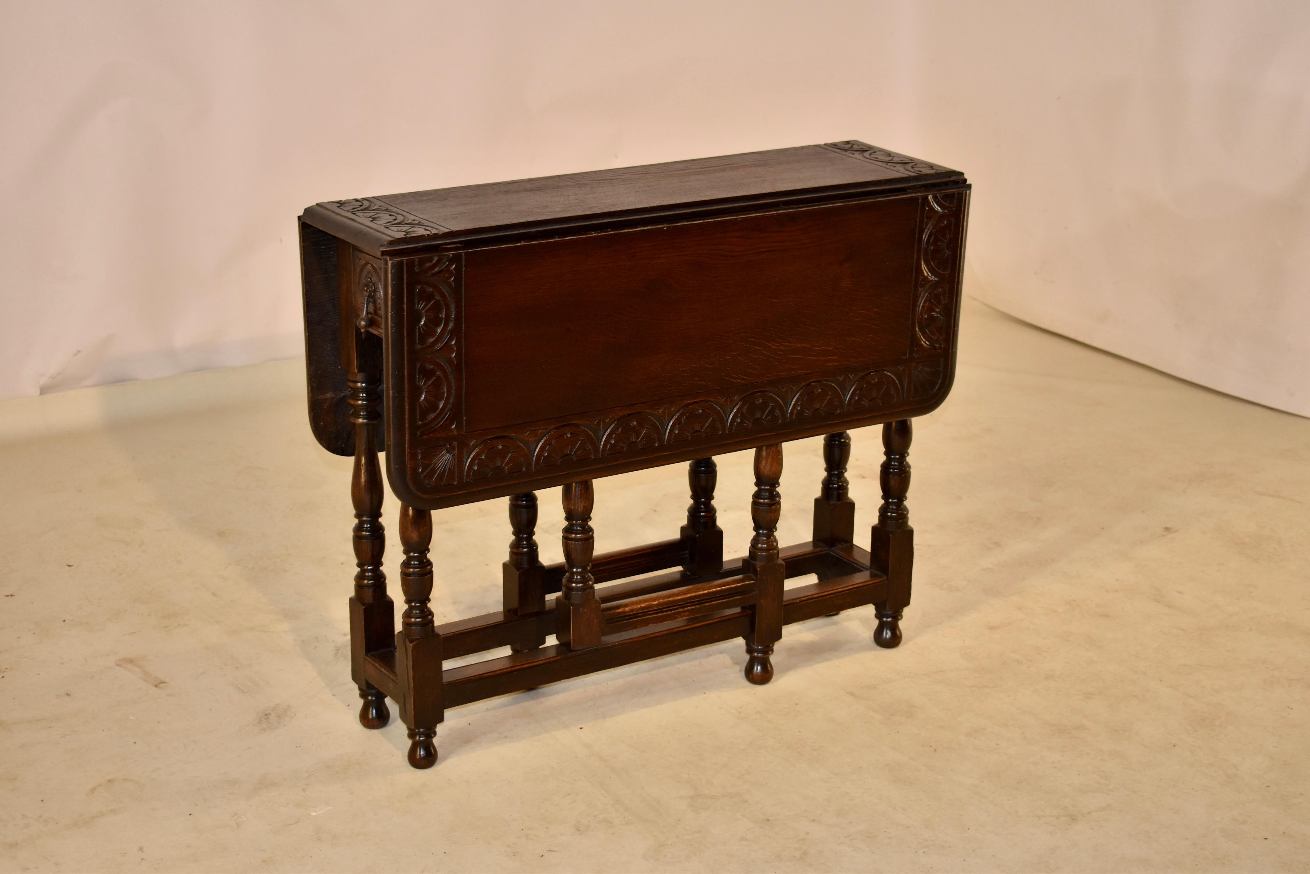 19th century oak gate leg table from England with a carved band on the top, surrounded by a beveled edge, following down to a simple apron containing a single small drawer on one end. The table is supported on hand turned legs, joined by simple