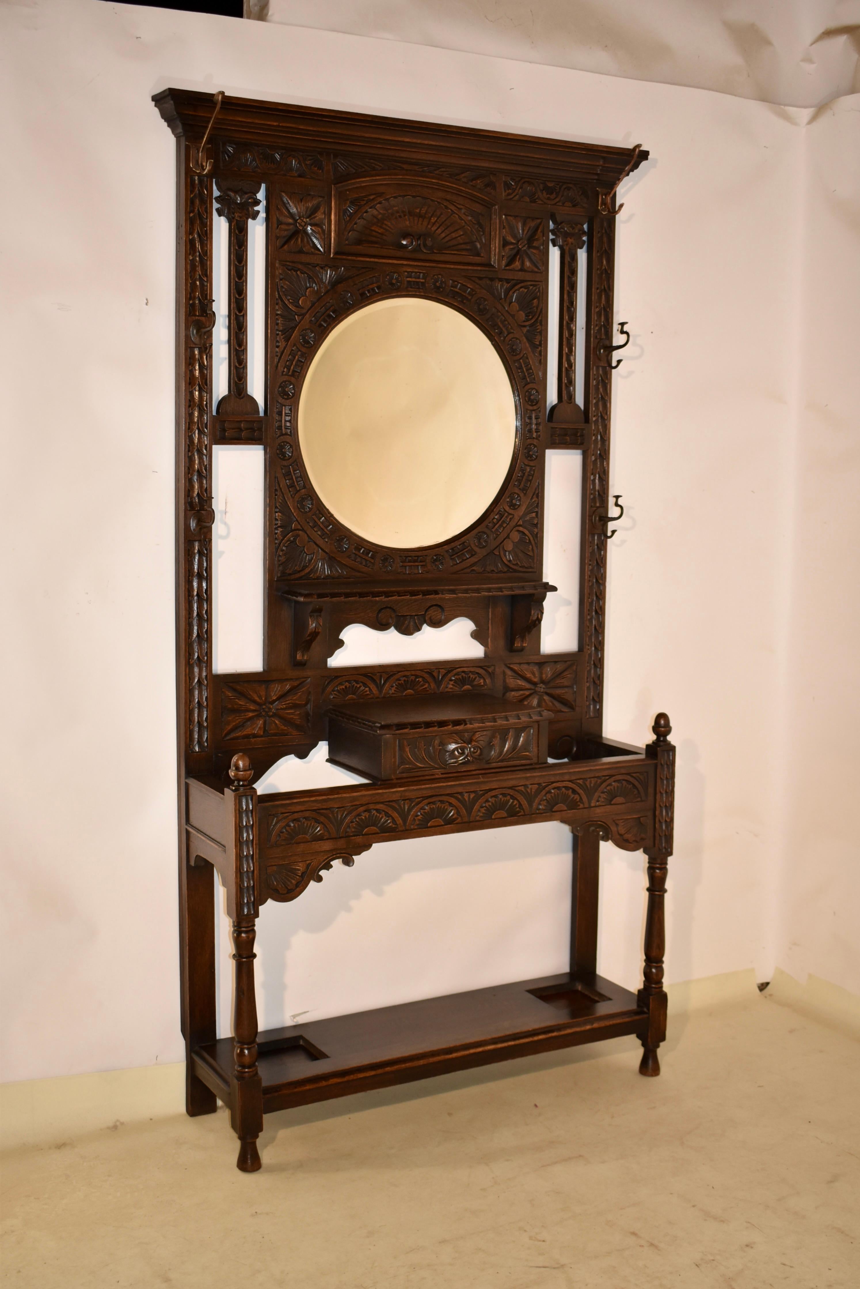 19th century oak hall stand from England.  The top has a lovely crown molding, over a hand carved central panel, flanked by carved sides, which have three brass hooks on each side for excellent hat or coat storage.  The central panel is wonderfully