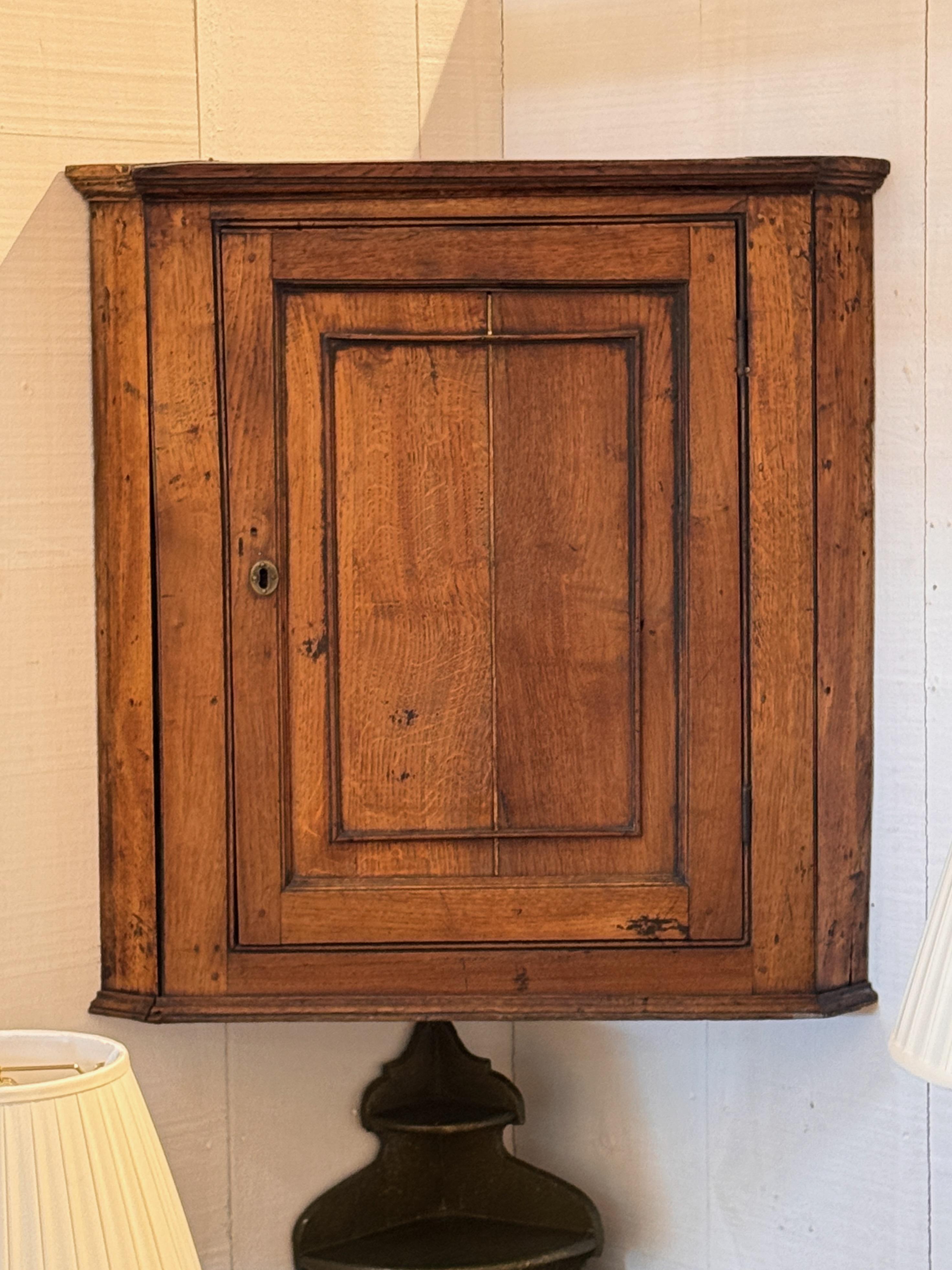 Armadio a muro compatto in Oak Oak con anta a pannelli e finitura calda originale. Presenta una modanatura semplice e un interno usurato e verniciato di rosso con scaffalature. I primi lavori di falegnameria e la costruzione a pioli sono visibili in