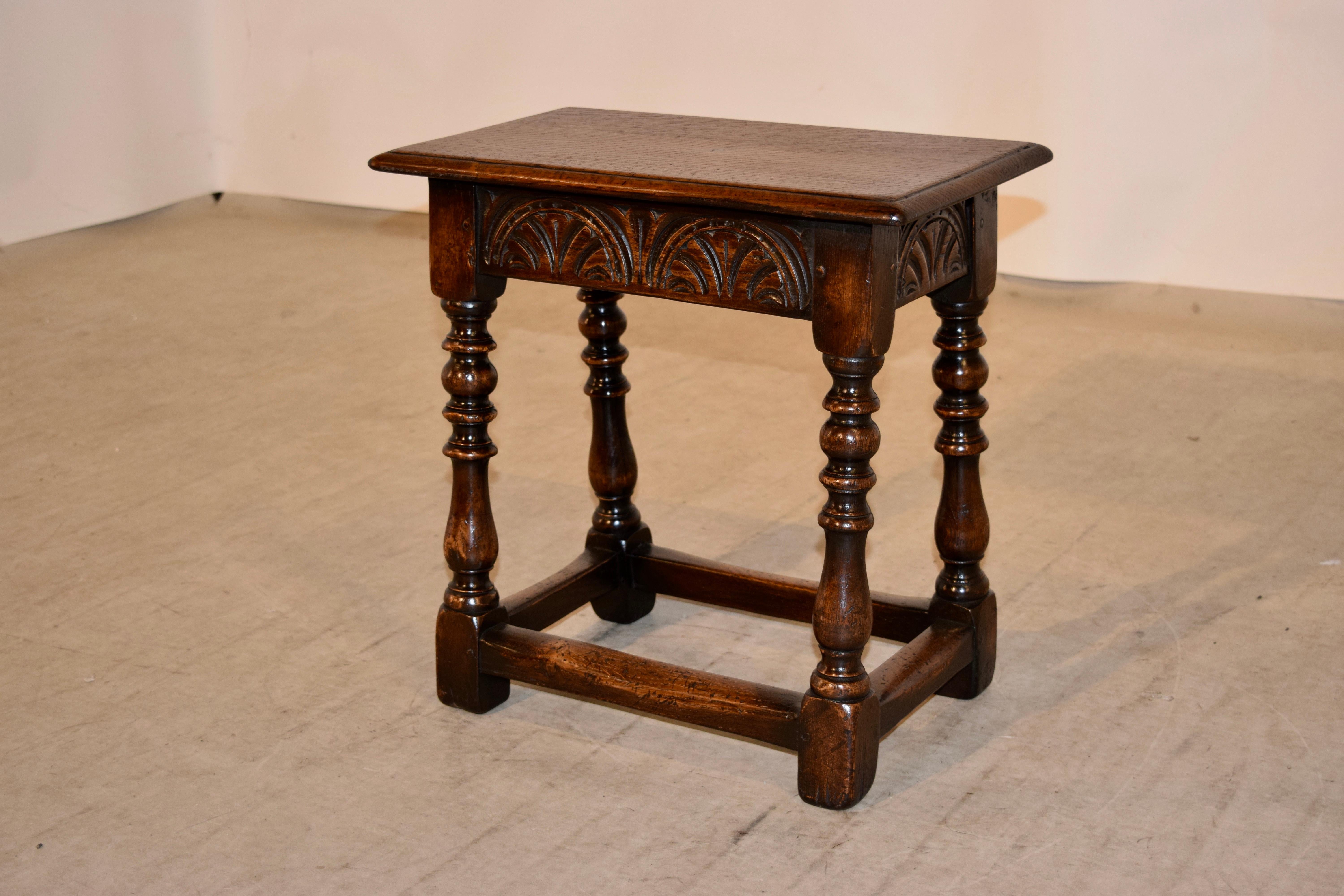 19th century oak joint stool from England with a beveled edge around the top following down to a hand carved decorated apron on all four sides and supported on hand-turned legs, which are joined by simple stretchers.