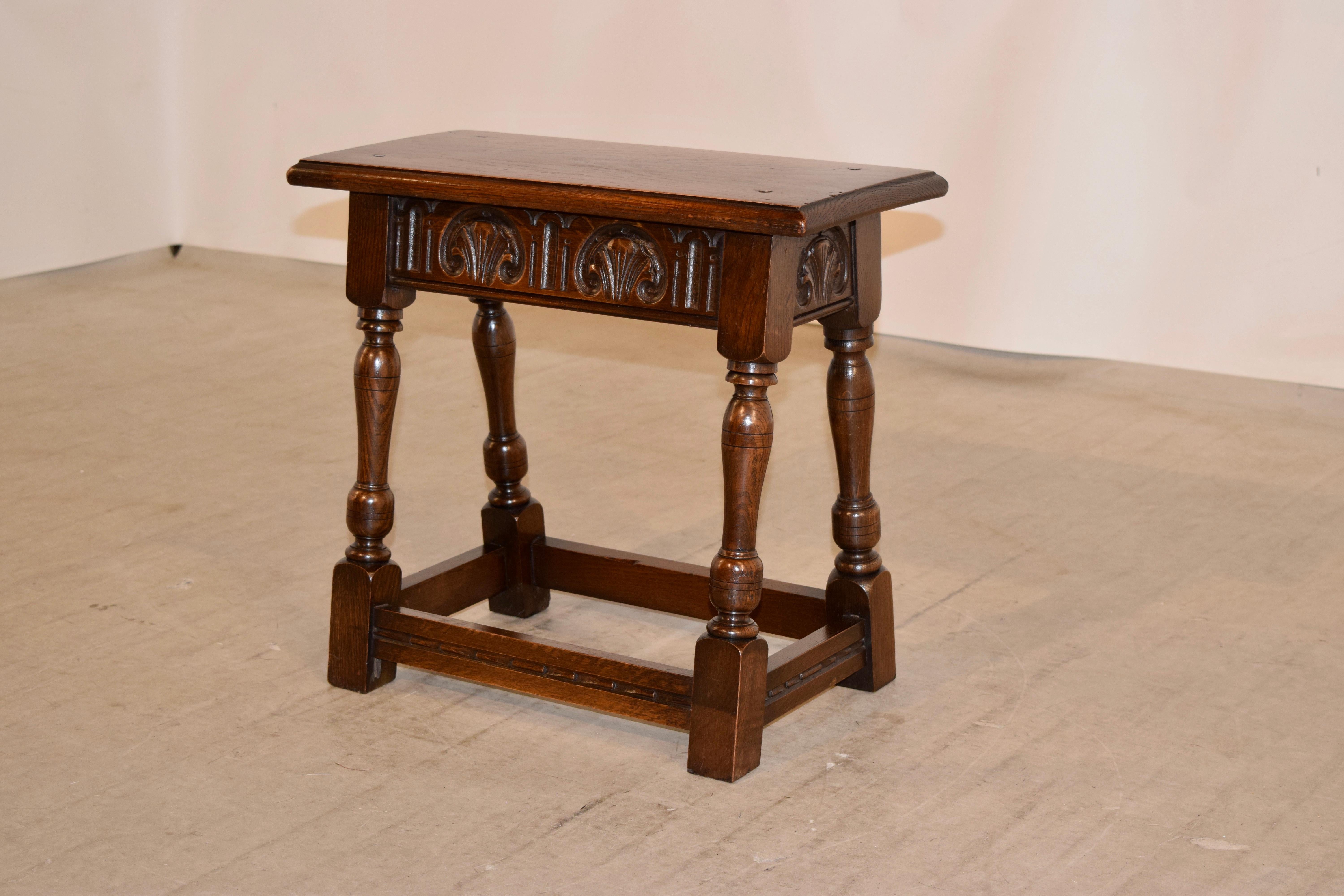 19th century English oak joint stool with pegged construction in the top and a beveled edge, following down to a hand carved apron on all four sides, for easy placement in any room and supported on hand-turned and splayed legs joined by routed and