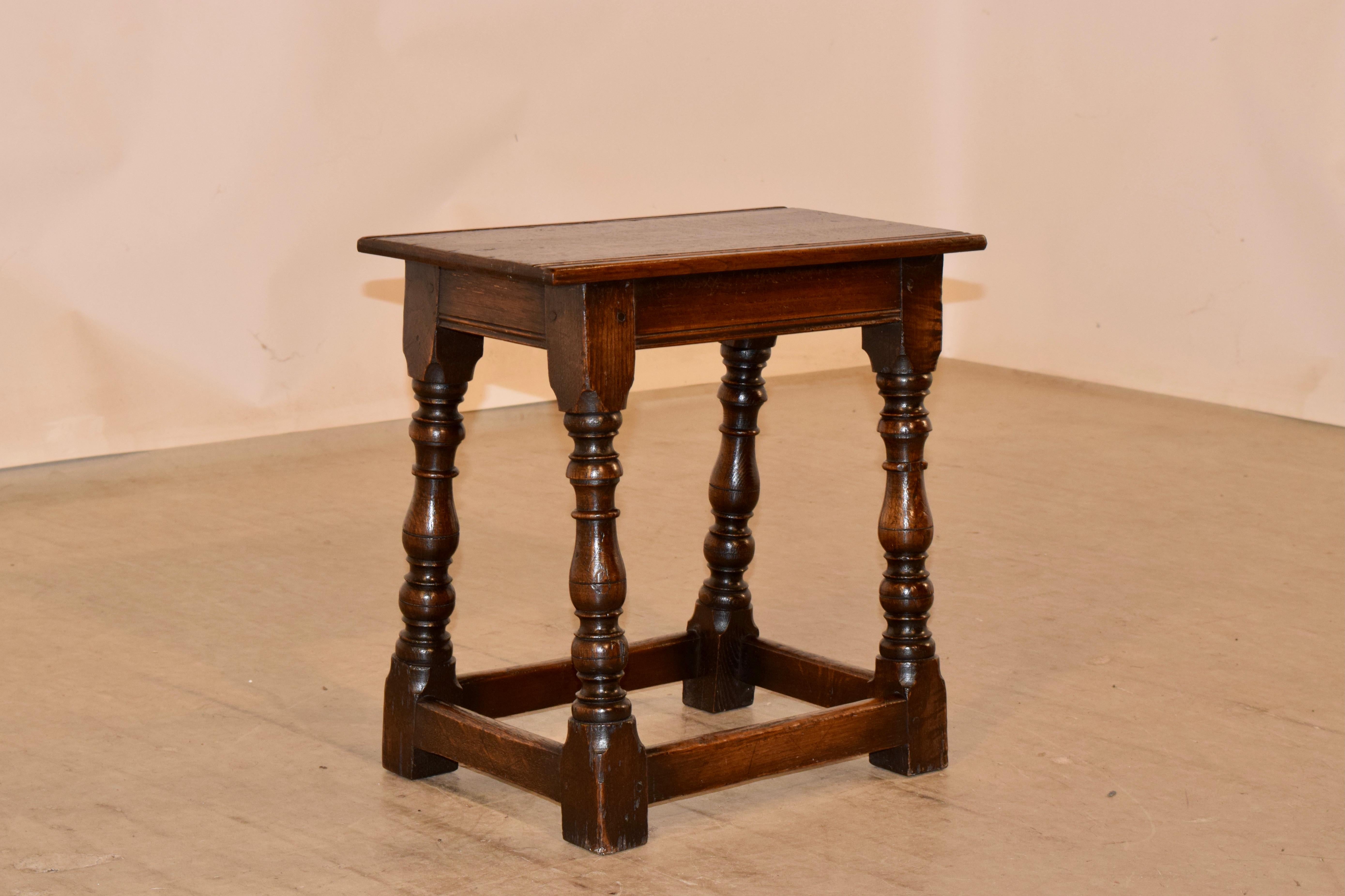 19th century oak joint stool from England with a routed edge on the top, following down to a simple apron also with routed detail along the edge and supported on hand turned splayed legs, joined by simple stretchers.