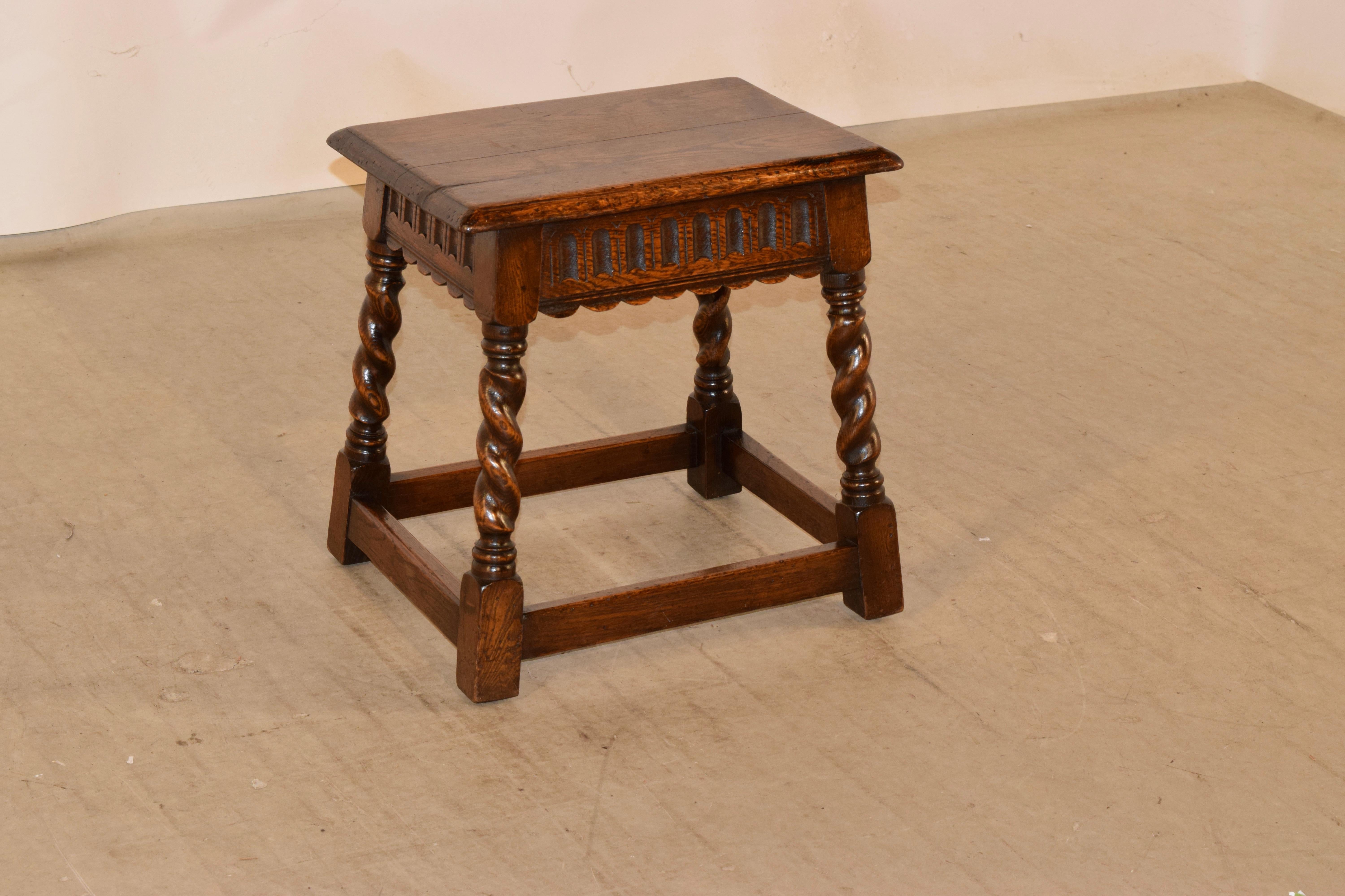 19th century oak stool from England with a beveled edge around the top over a hand carved and scalloped apron and supported on hand turned barley twist splayed legs, joined by simple stretchers.