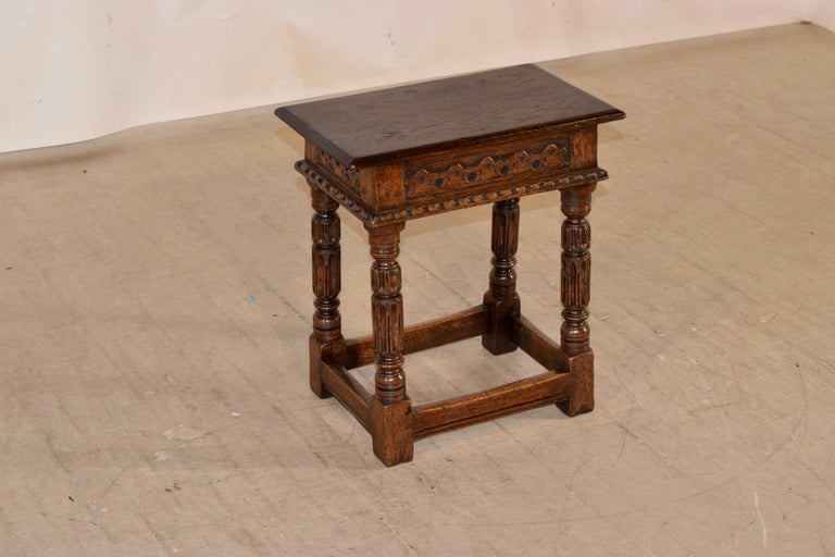 19th century oak joint stool from England with a single plank seat, which has beveled edges and is sitting atop a wonderfully hand carved decorated apron which finishes with a carved molded edge, and supported on hand turned and carved legs. the