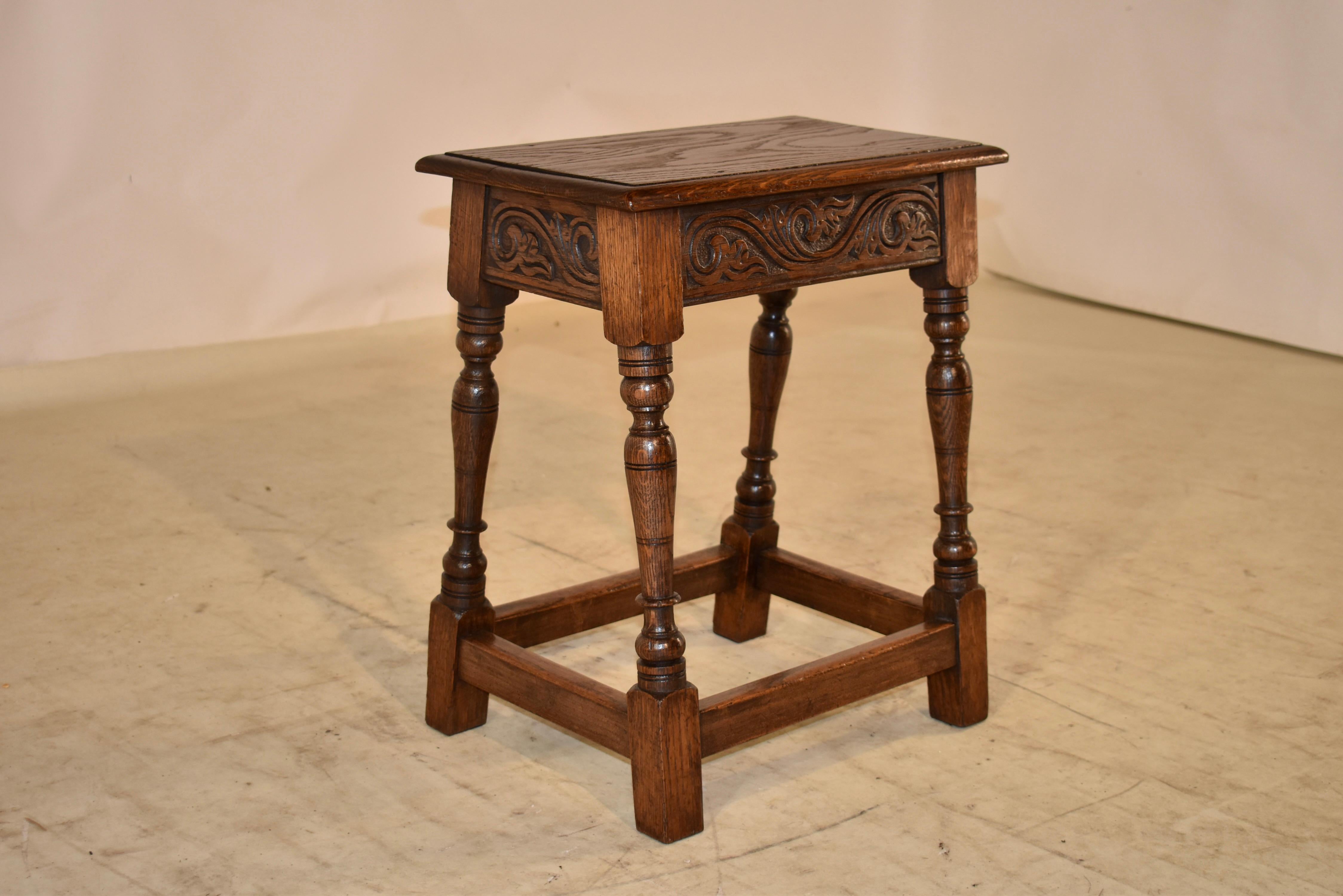 19th Century oak joint stool from England. The top is wonderfully figured and has a beveled edge, following down to a hand carved decorated apron. The stool is supported on hand turned and splayed legs, joined by simple stretchers.