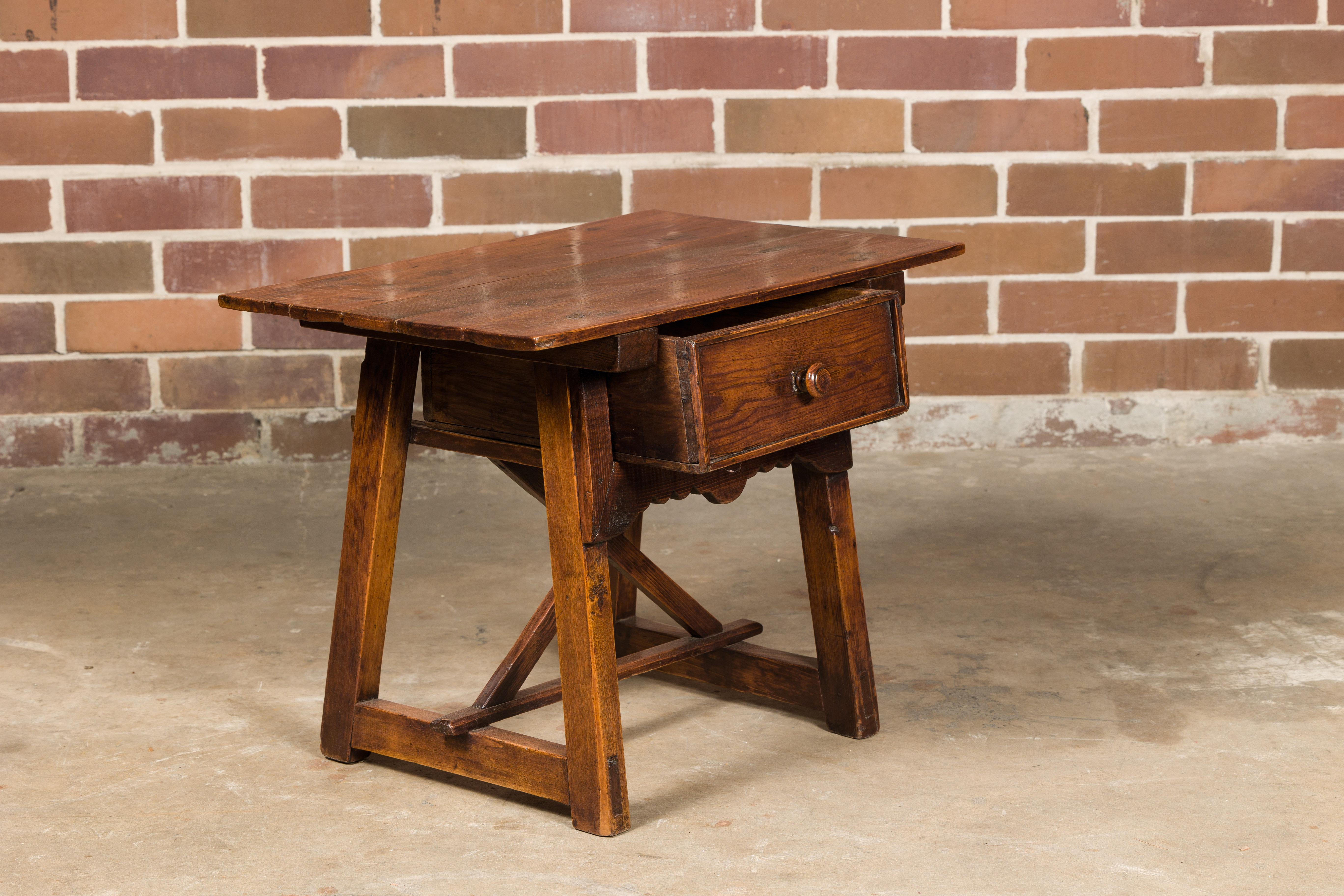 An English oak low side table from the 19th century with single drawer, carved apron and A-Frame base. This 19th-century English oak low side table exudes rustic charm and timeless elegance. Crafted from oak, it showcases a beautiful patina that