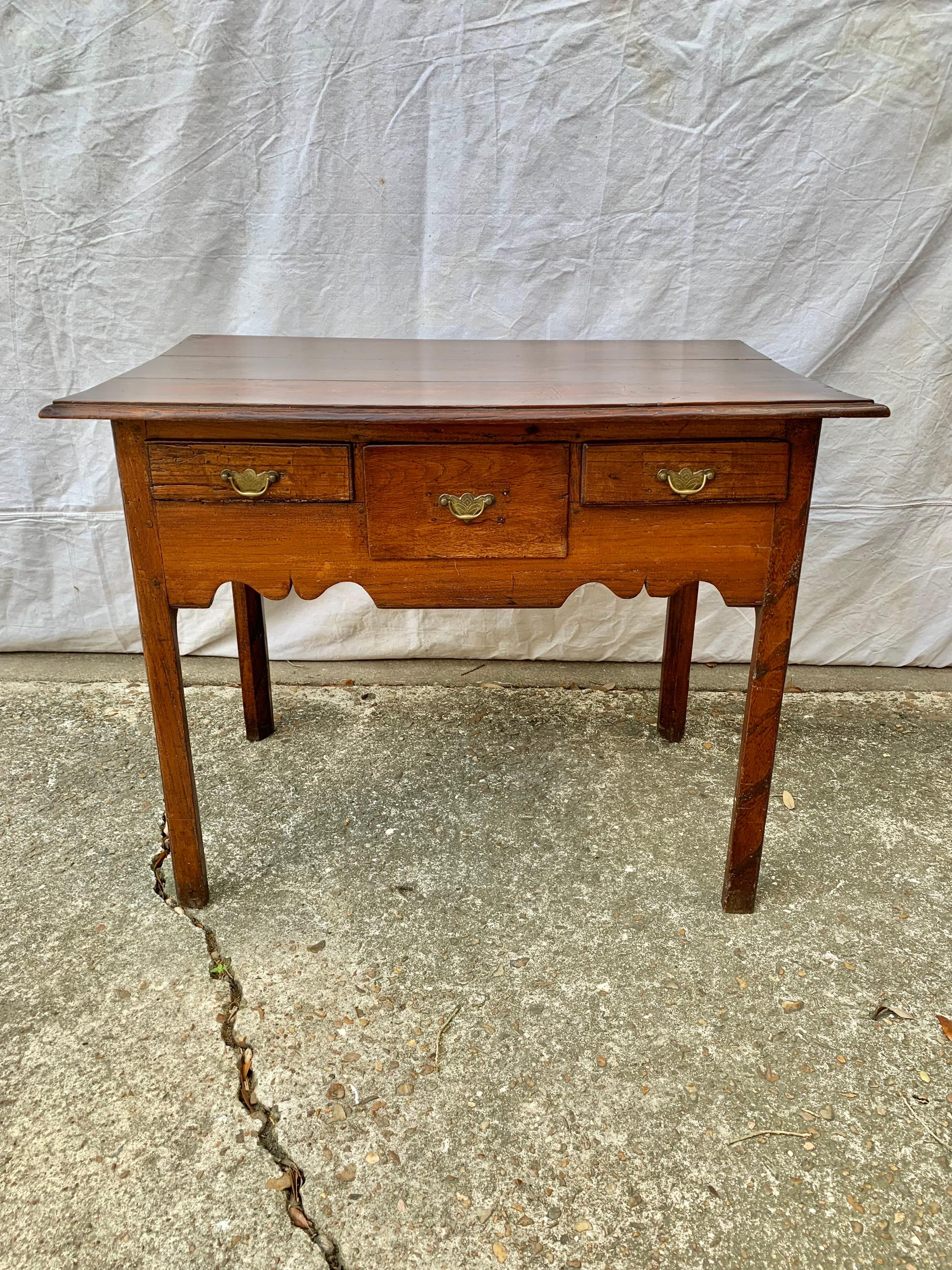 Found in England, this side table was crafted from old growth oak by English artisans in the 1800's. This table, often called a lowboy, features a rectangular three plank top above three drawers and the entire piece rest on four carved legs. The