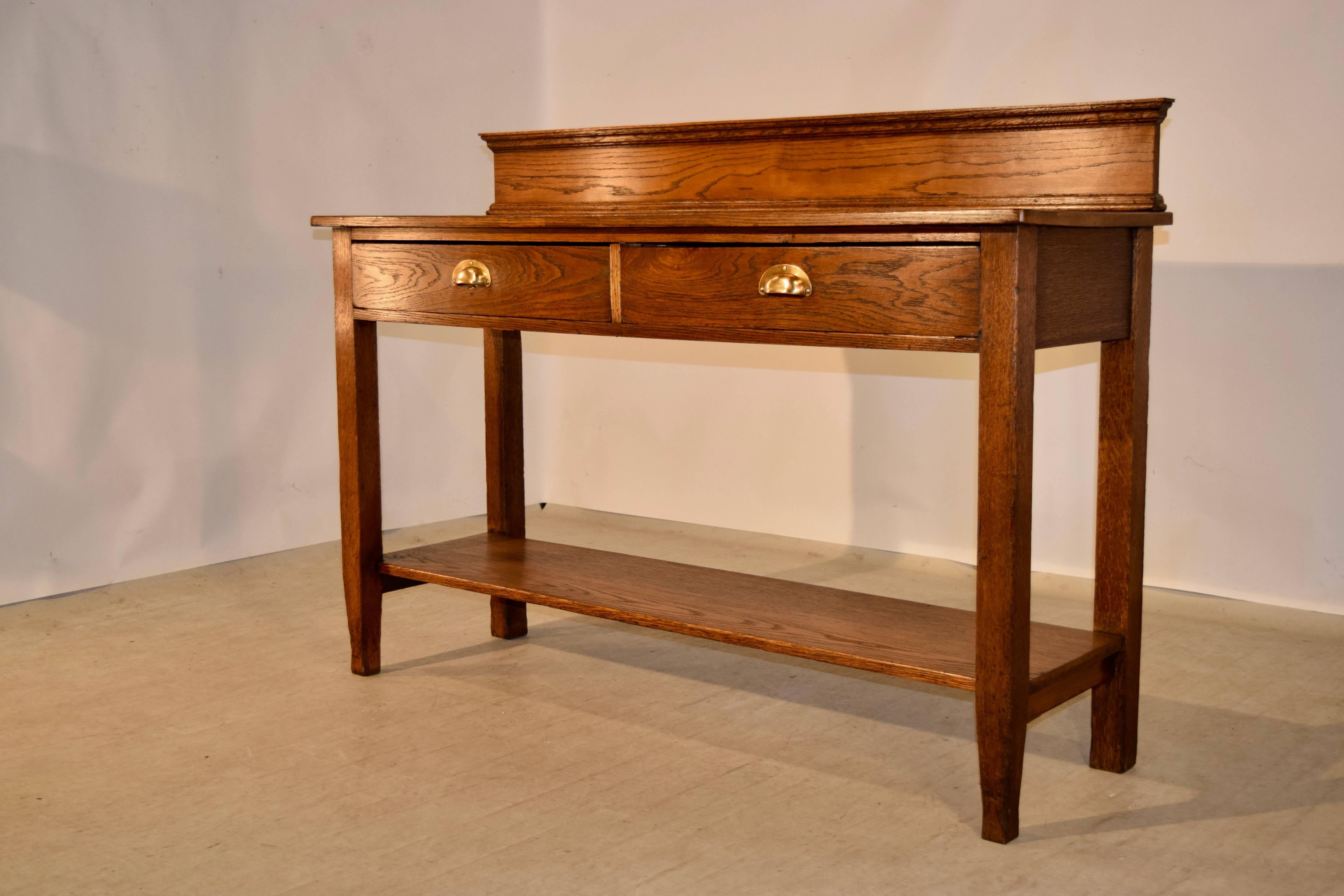 19th century simple oak server from England. There is a backsplash with molded decorated edges following down to a simplistic server with two drawers and tapered legs, which are joined by a lower shelf. Measure: The serving height is 35.88 inches.