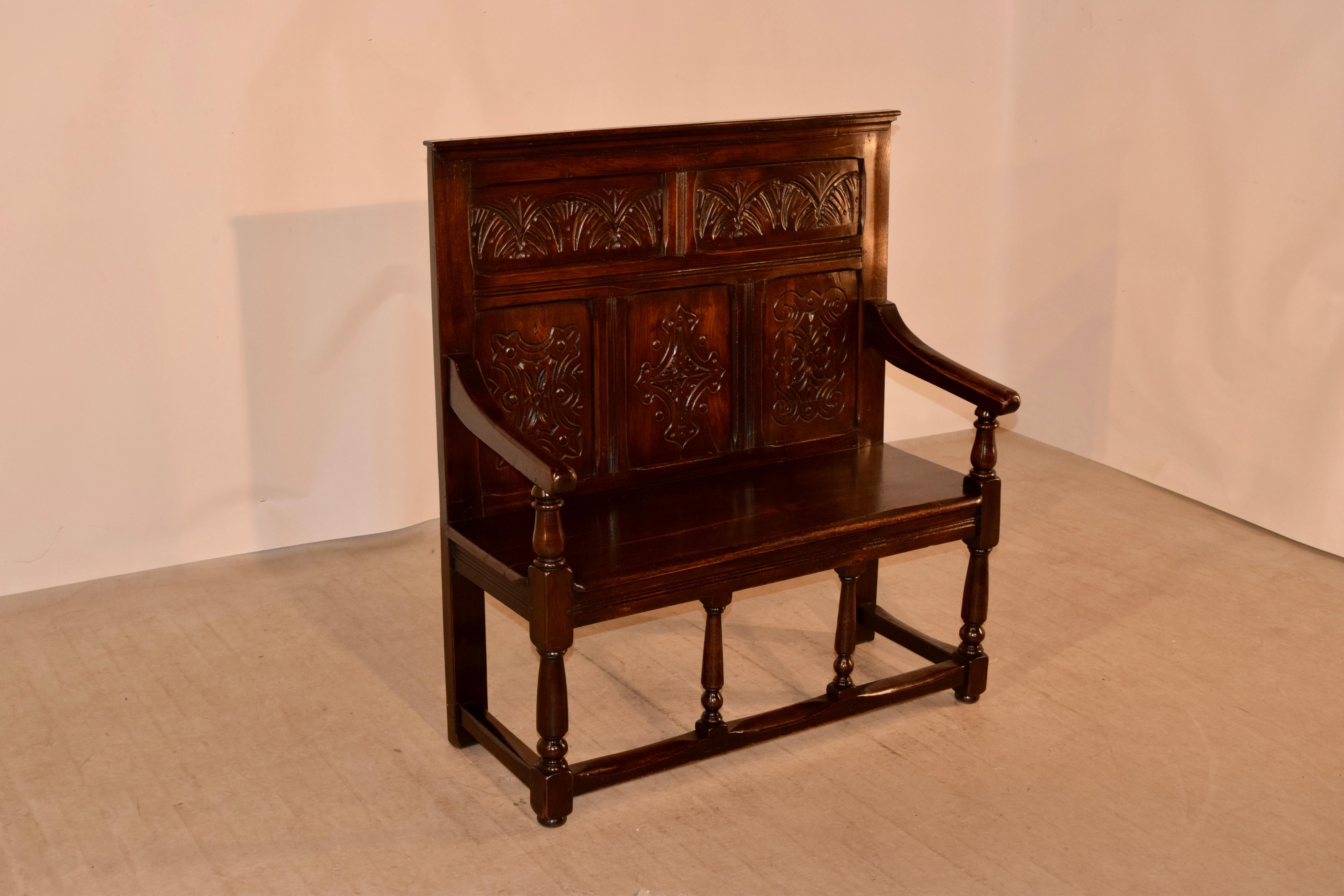 19th century English oak settle with a molded edge at the top following down to two over three hand carved panels in the back, supported on a base with hand-turned supports and simple stretcher.