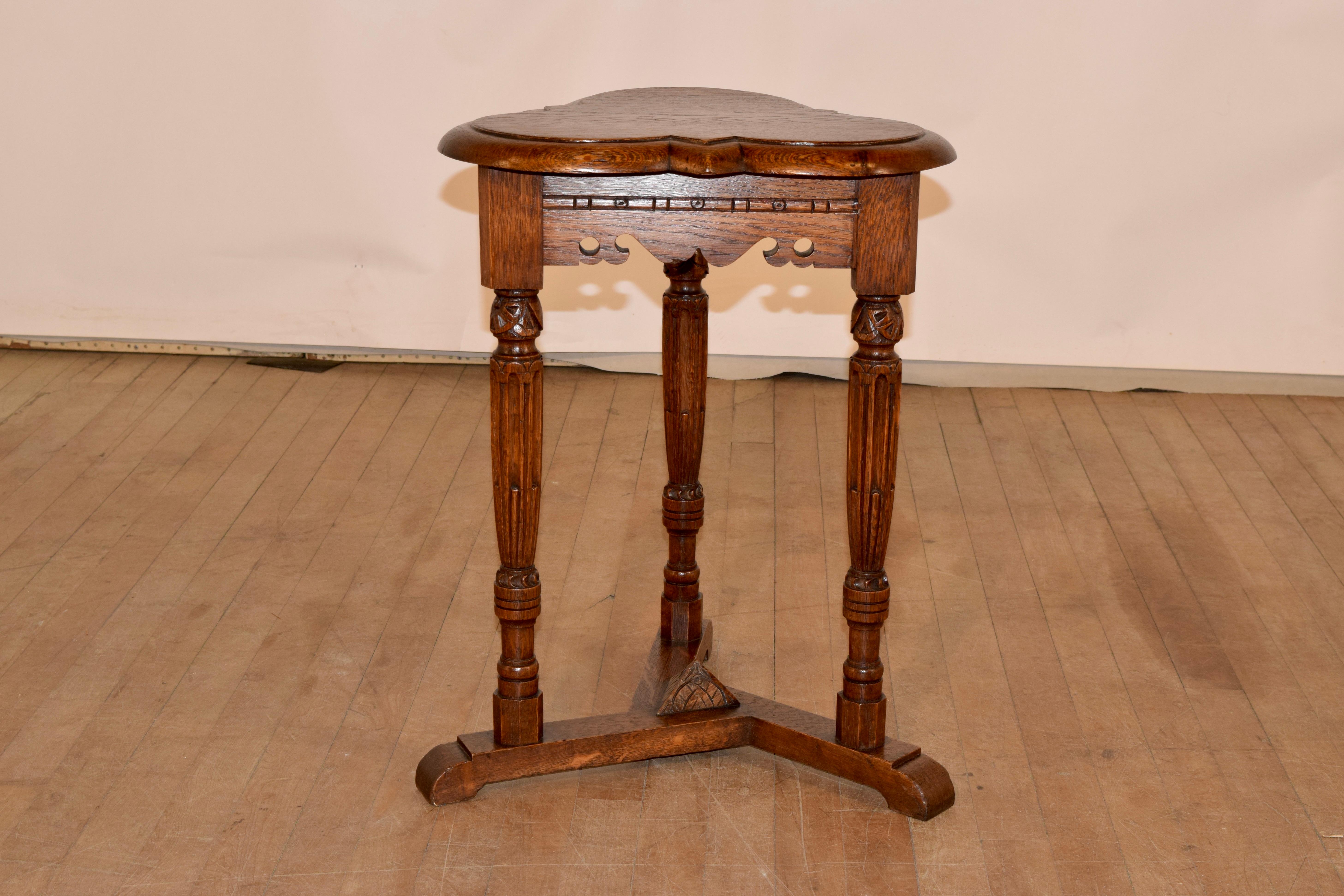 19th century oak side table from England with a scalloped and beveled edge around the top, following down to a scalloped and pierced apron. the table is supported on hand turned and carved fluted legs, over a tripod base, which is enhanced by a