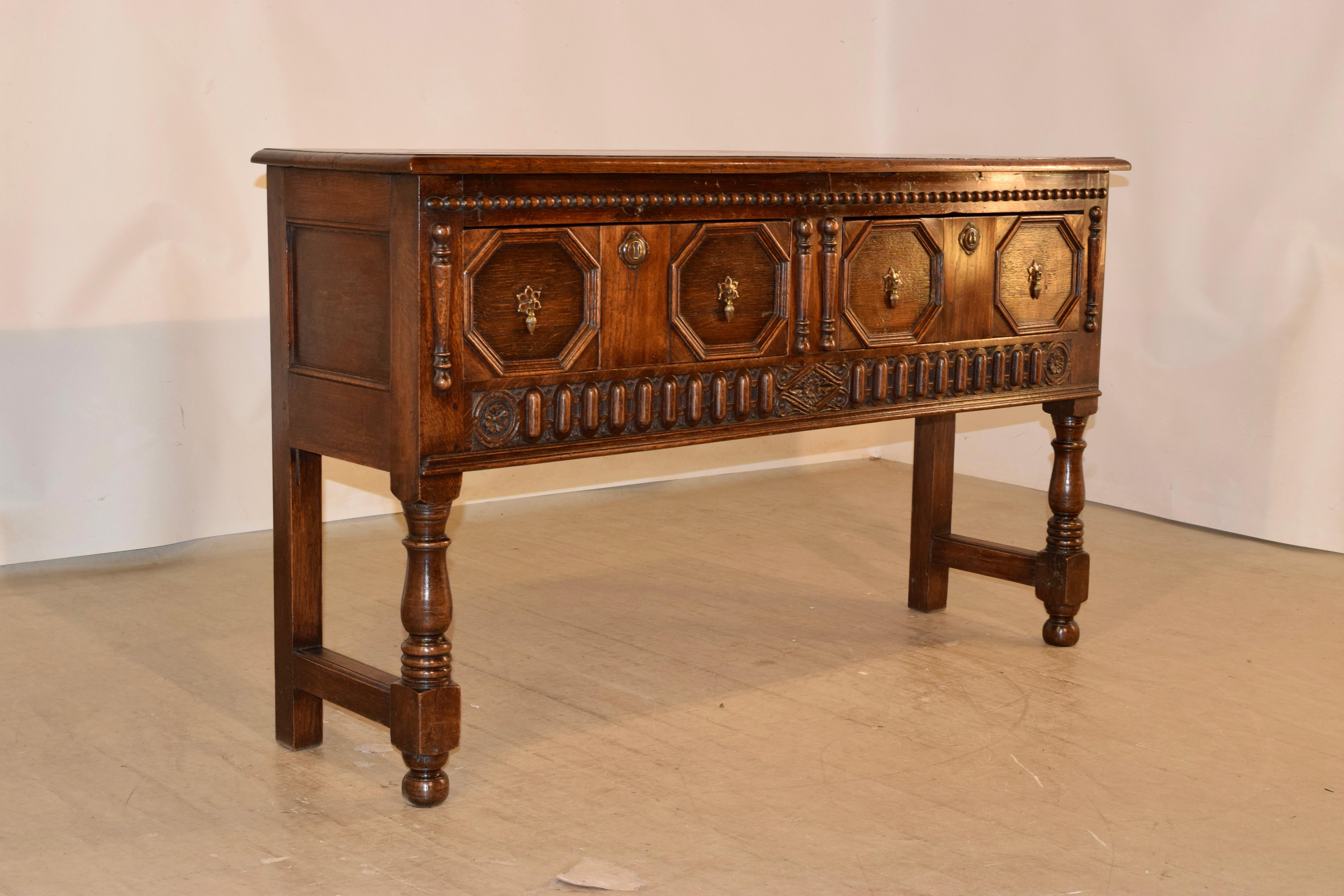 19th century oak sideboard from England with a beveled edge around the top, following down to paneled sides and two drawers in the front with raised geometric panels, flanked by hand-turned applied moldings and a beaded molding across the top. The