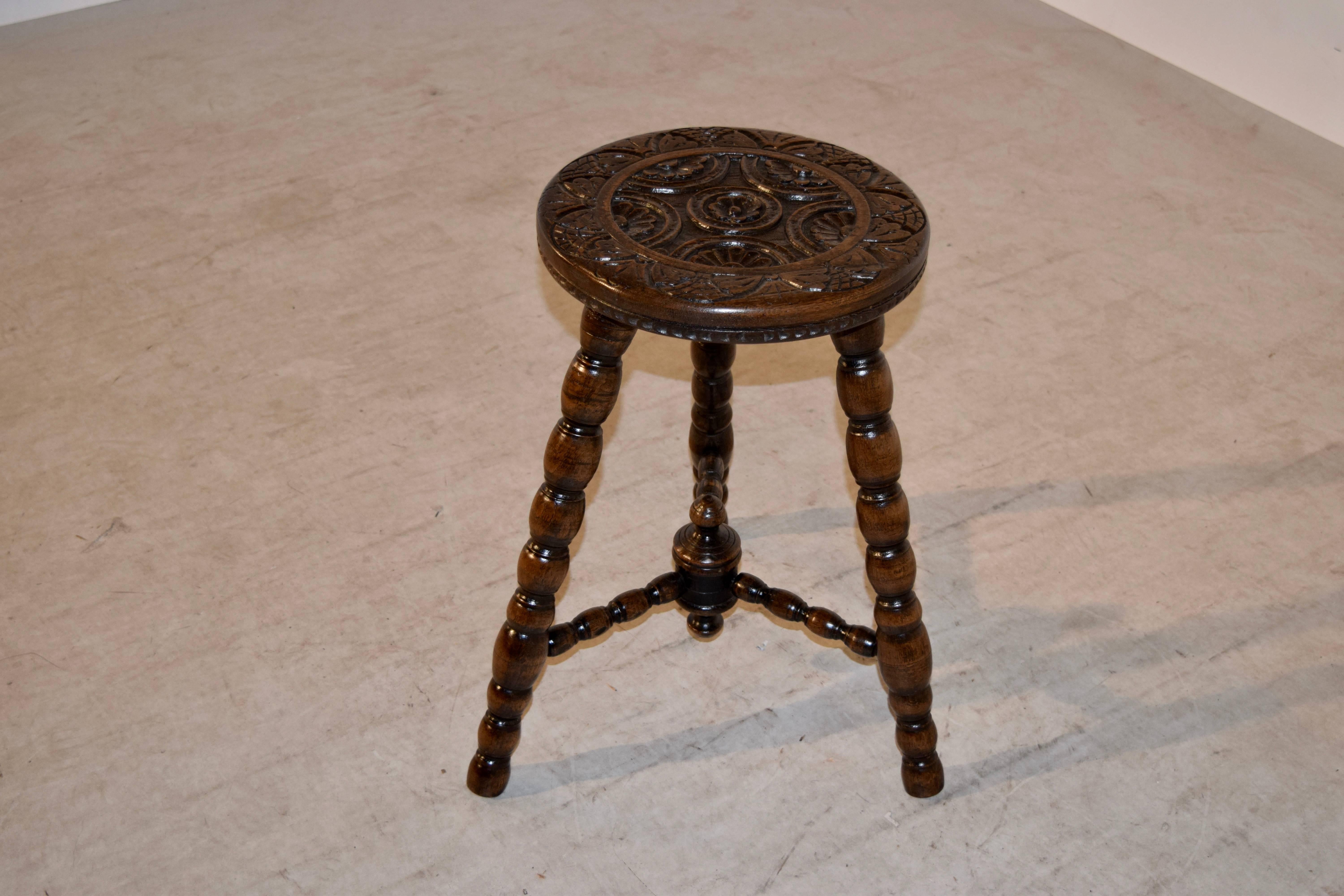 19th century English oak stool with a hand-carved decorated top, supported upon hand-turned spool legs, joined by matching stretchers, finished with a finial. The seat diameter is 12 inches.