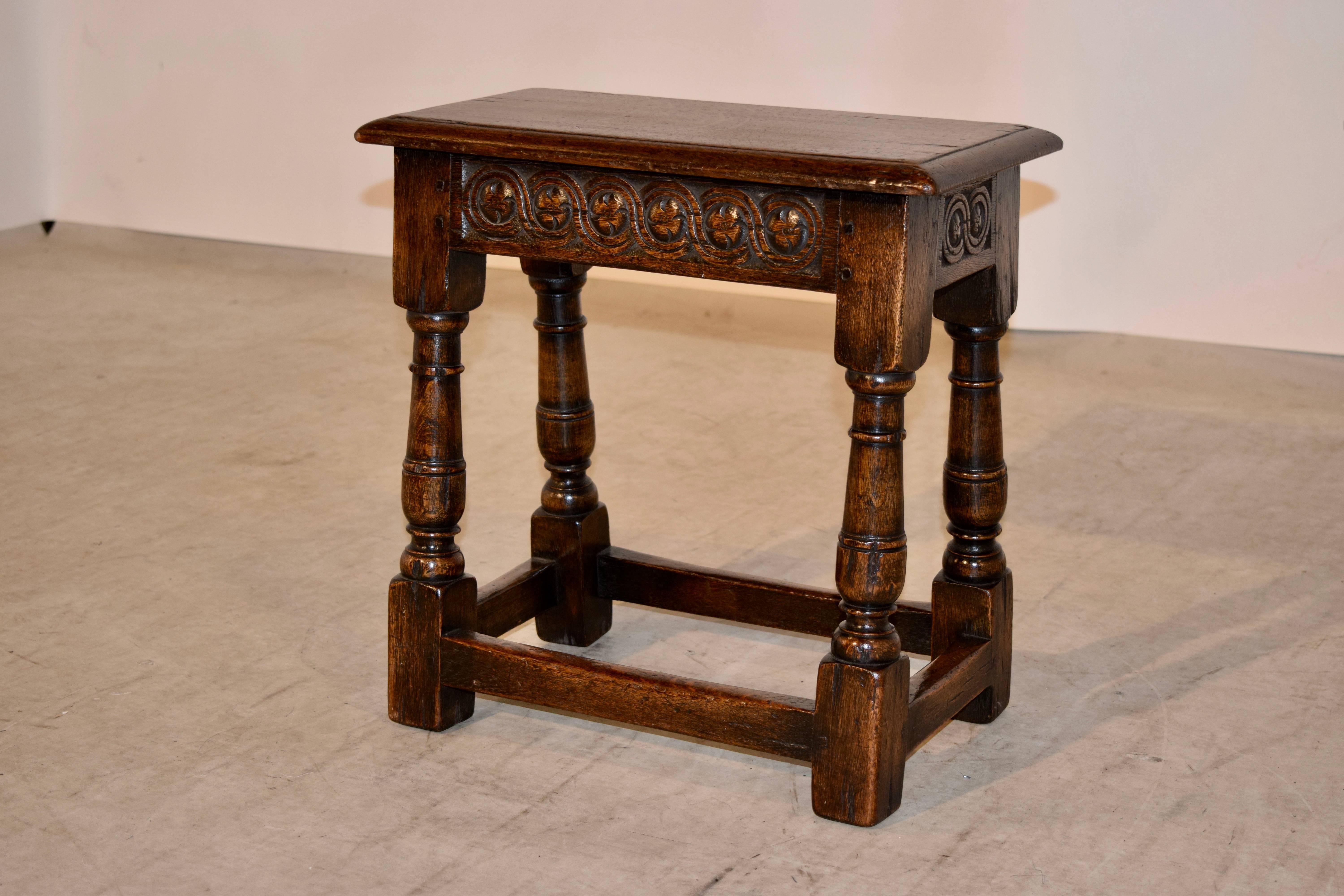 19th century English oak joynt stool with a beveled edge around the top, following down to a hand-carved decorated apron on all four sides and hand turned legs, which have slight losses to the turned collars. The legs are joined by simple