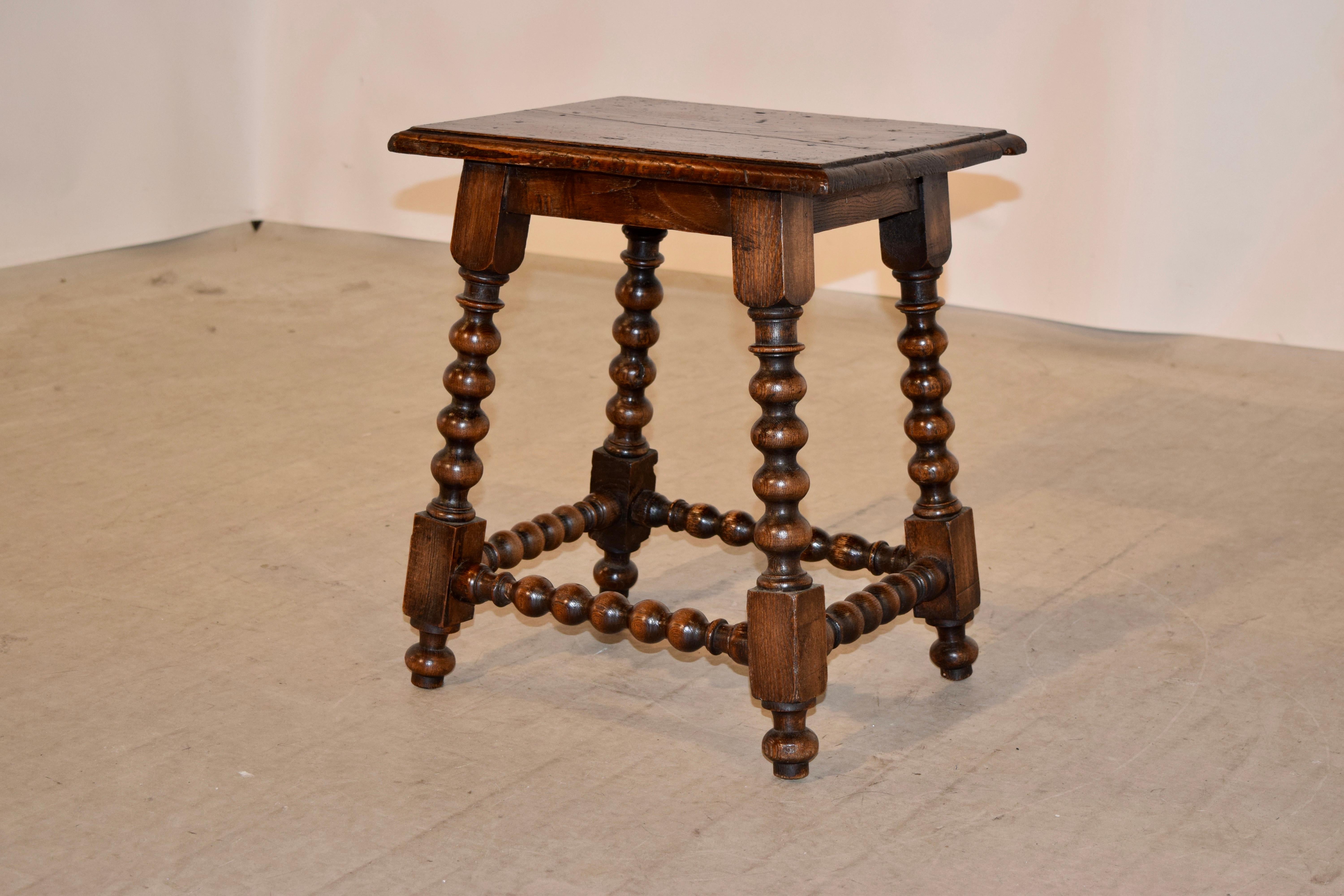 19th century oak stool from England with a beveled edge around the top following down to a simple apron and splayed legs which are hand-turned and are connected by matching stretchers. Raised on hand-turned feet.