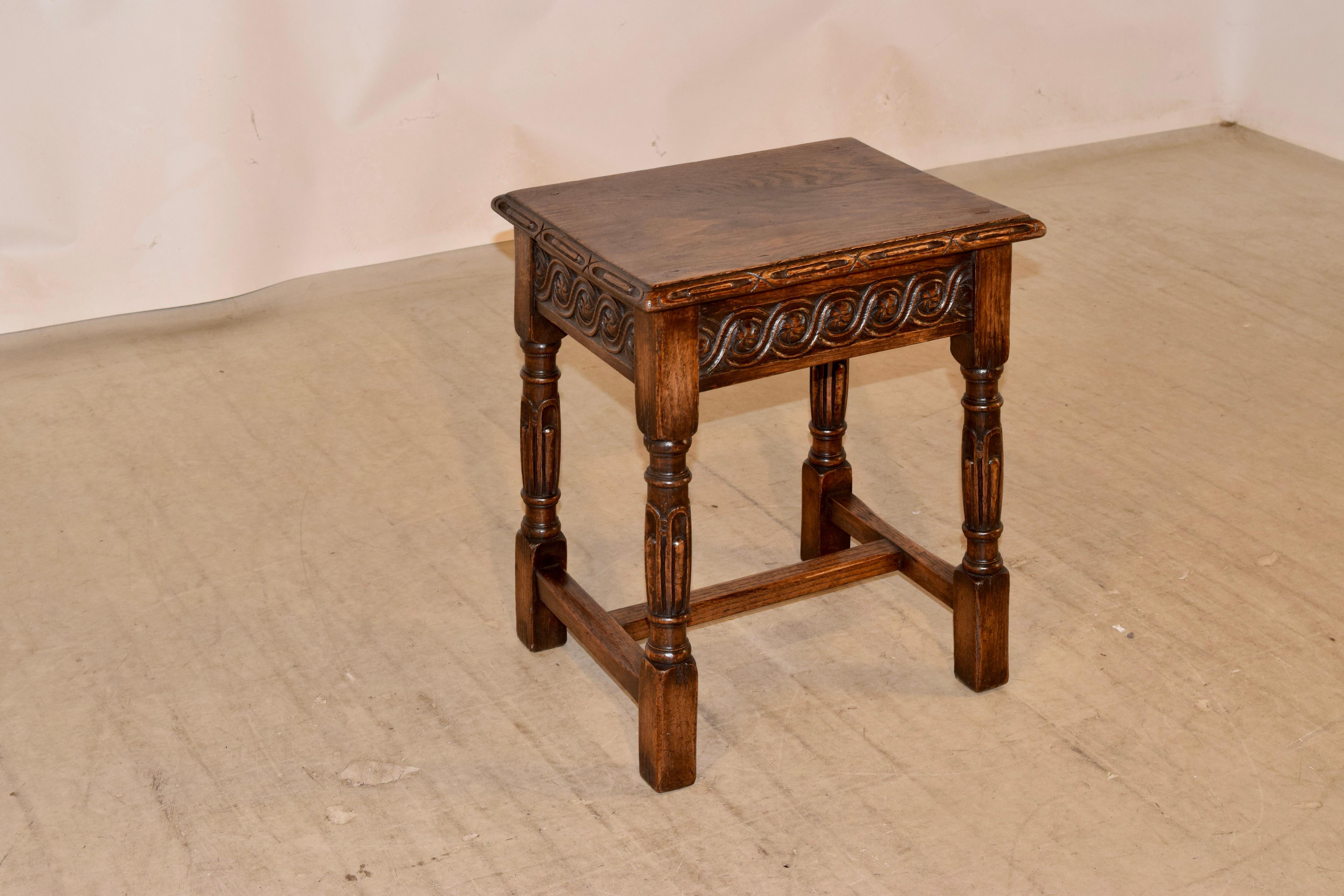 19th century English oak stool with a wonderfully hand carved and beveled edge around the top, over a carved decorated apron and supported on hand turned and carved legs, joined by simple stretchers.